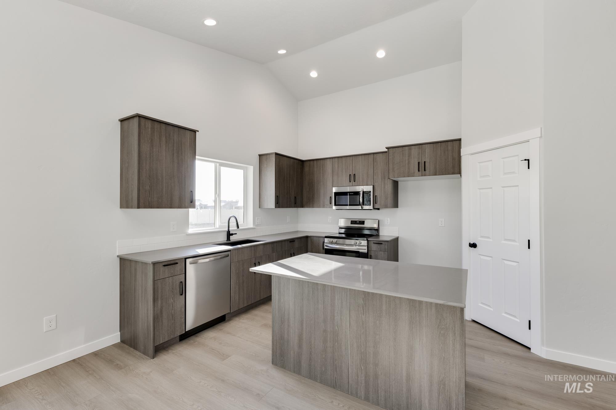 Kitchen with modern cabinets, a center island, appliances with stainless steel finishes, light wood-style flooring, and high vaulted ceiling