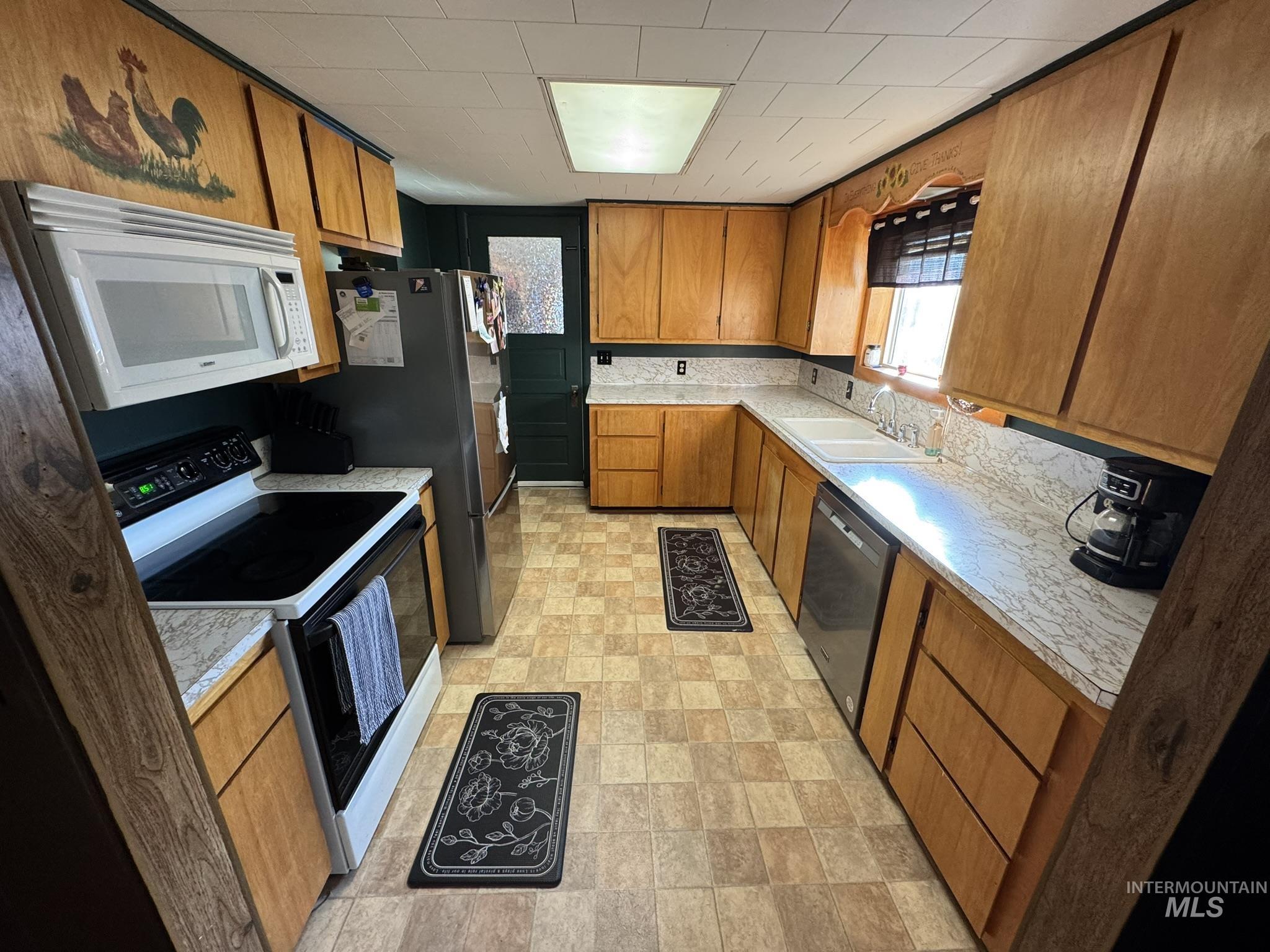 Kitchen with light countertops, white appliances, and brown cabinets
