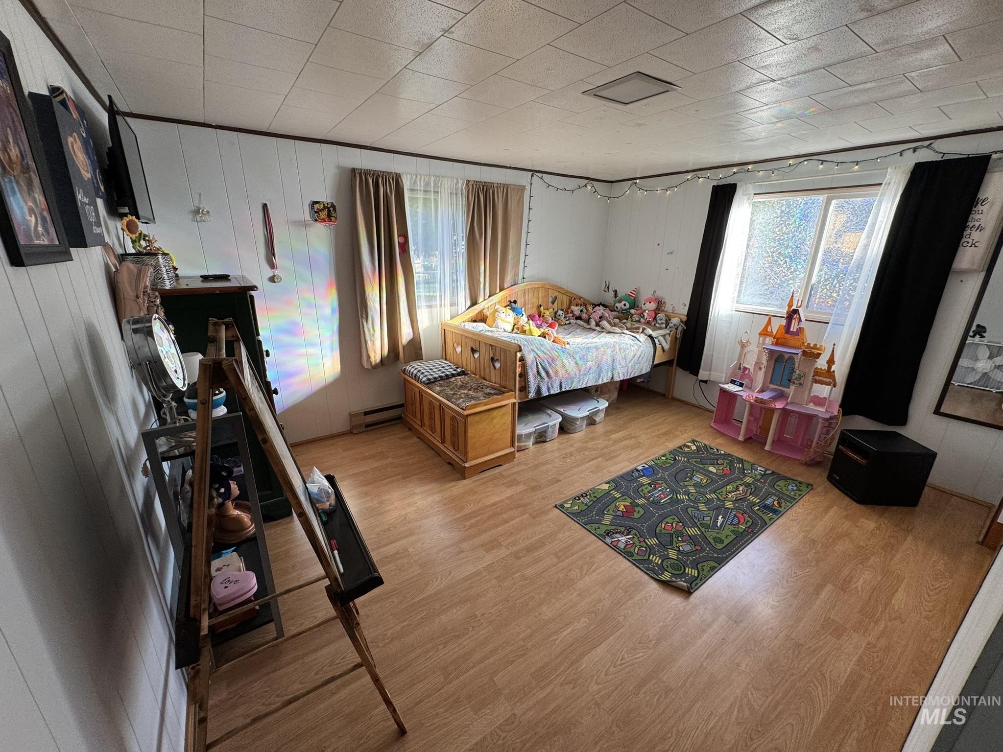 Bedroom featuring wood finished floors, wooden walls, and a baseboard radiator