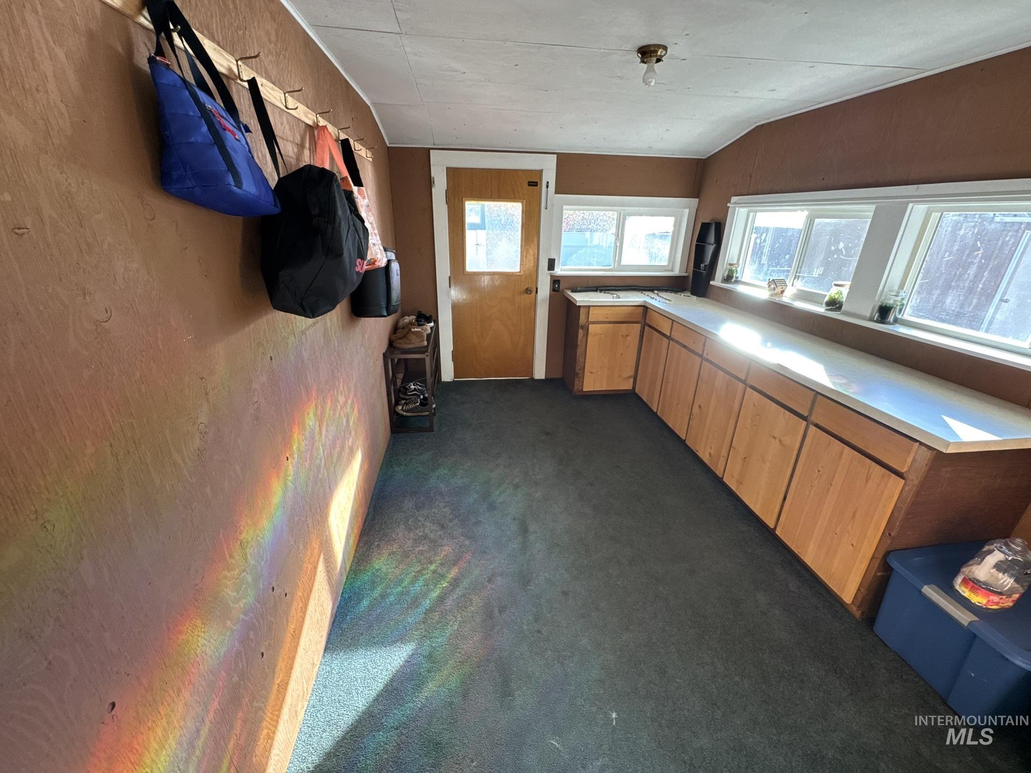 Kitchen with light countertops, dark colored carpet, brown cabinets, and vaulted ceiling