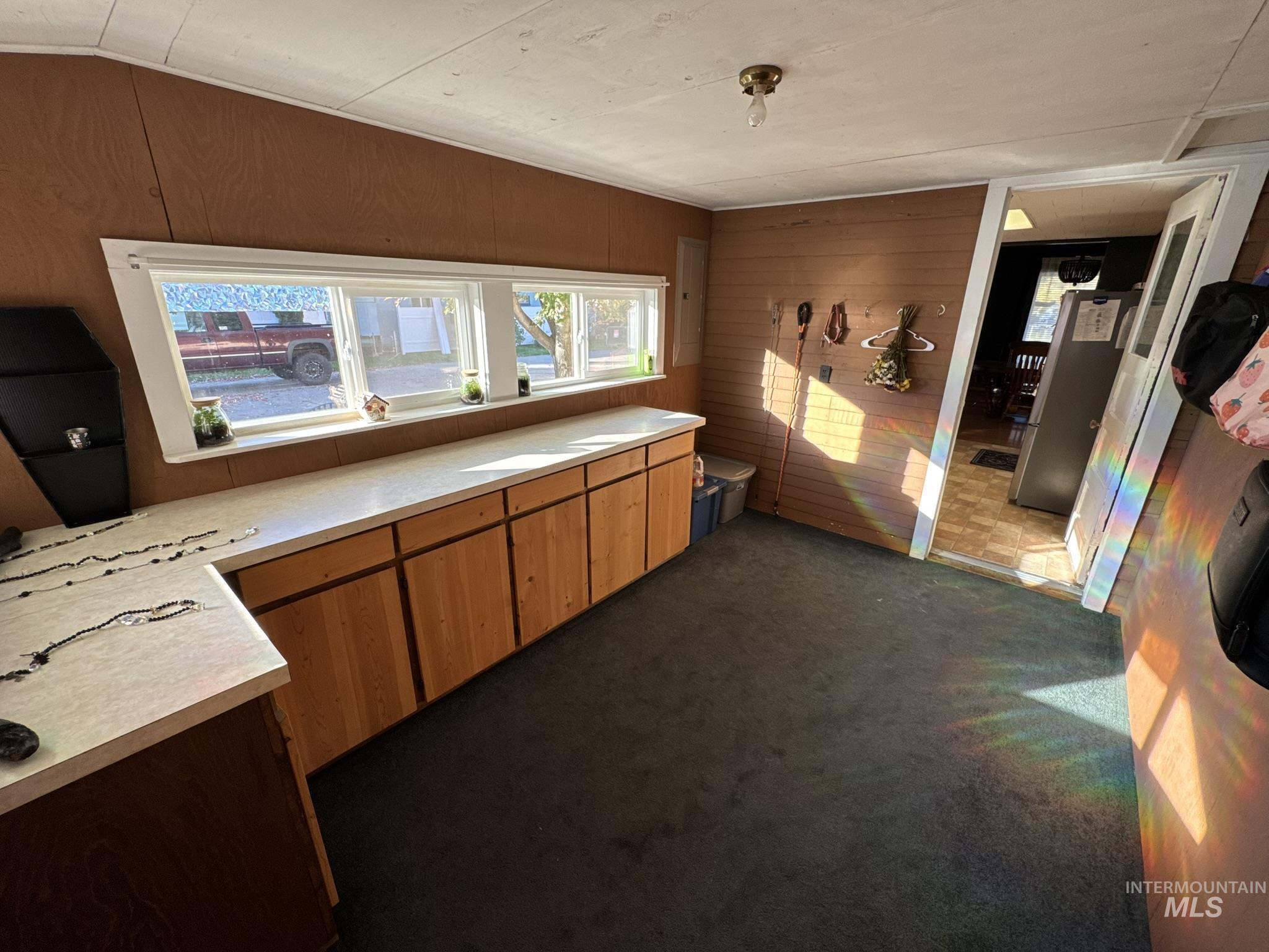 Kitchen featuring light countertops, wood walls, dark colored carpet, and brown cabinets