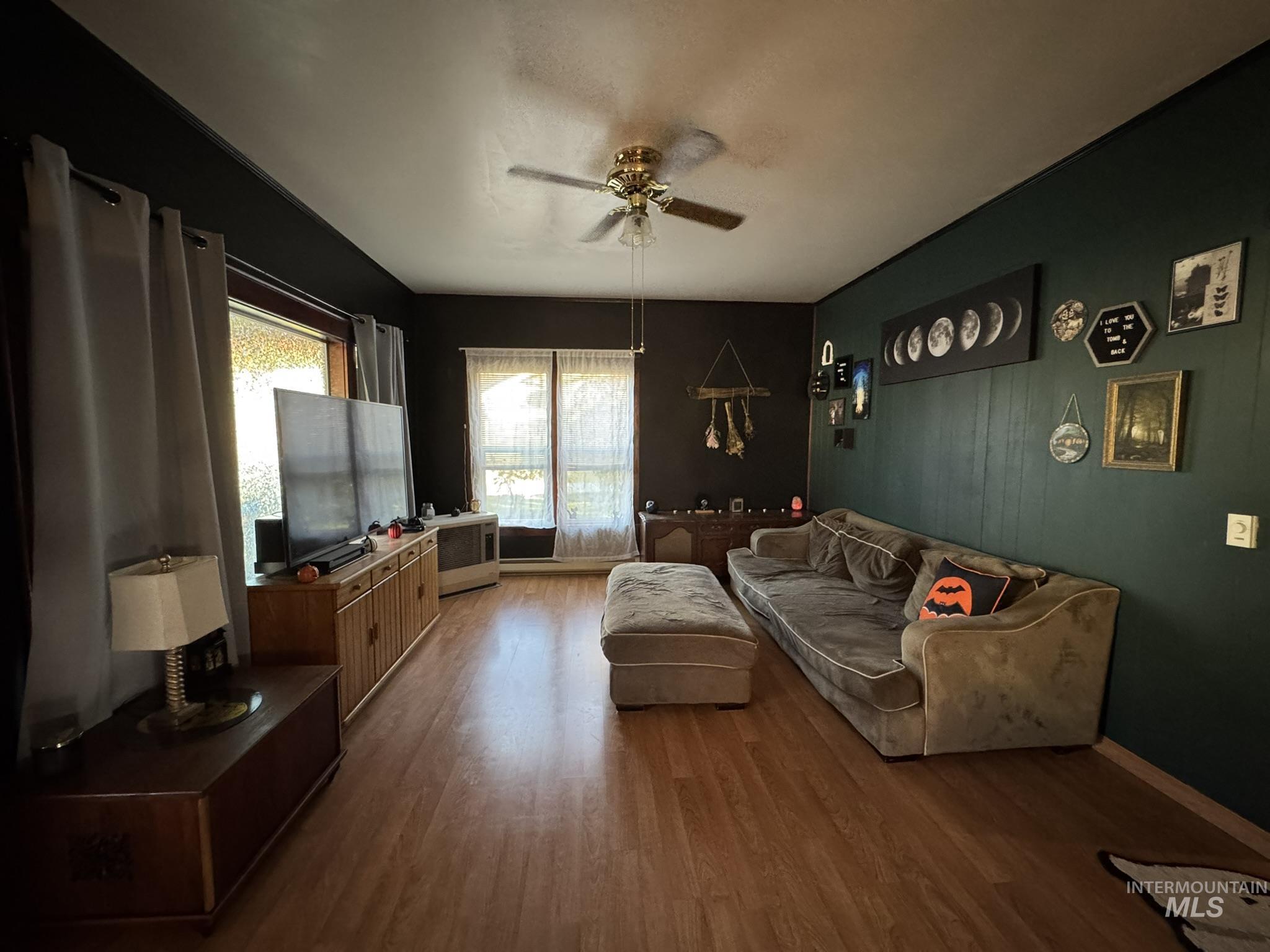 Living area featuring a ceiling fan, wood finished floors, and radiator heating unit