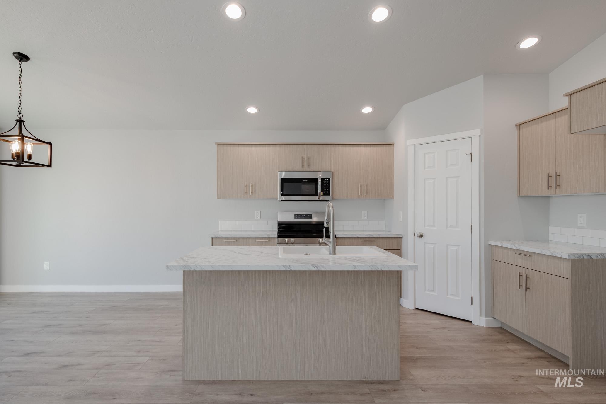 Kitchen with an island with sink, appliances with stainless steel finishes, light wood-style floors, light brown cabinets, and recessed lighting