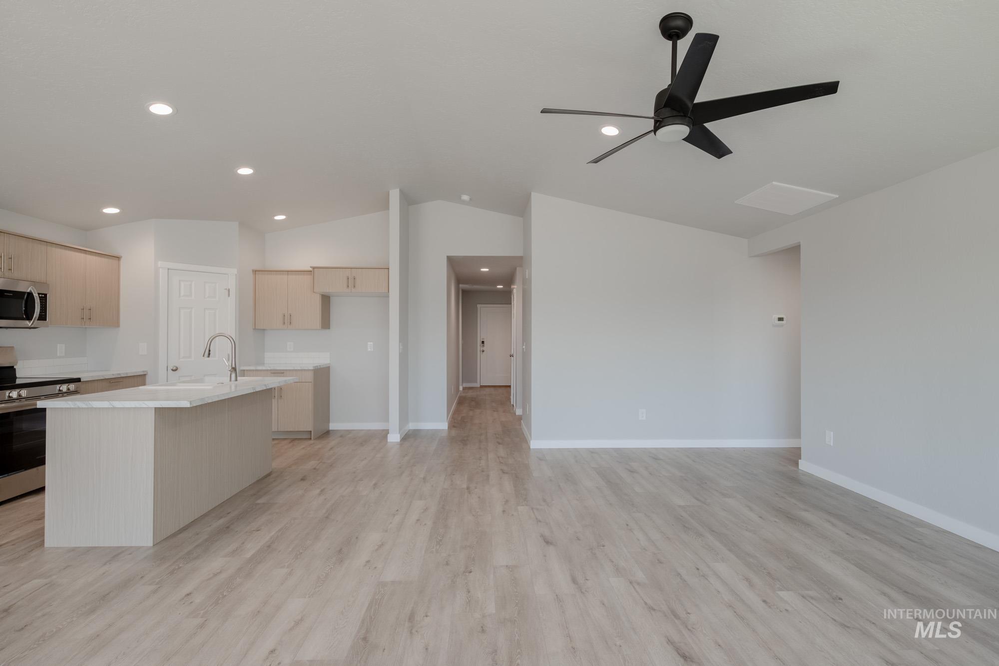 Kitchen featuring an island with sink, appliances with stainless steel finishes, vaulted ceiling, light wood-style flooring, and open floor plan