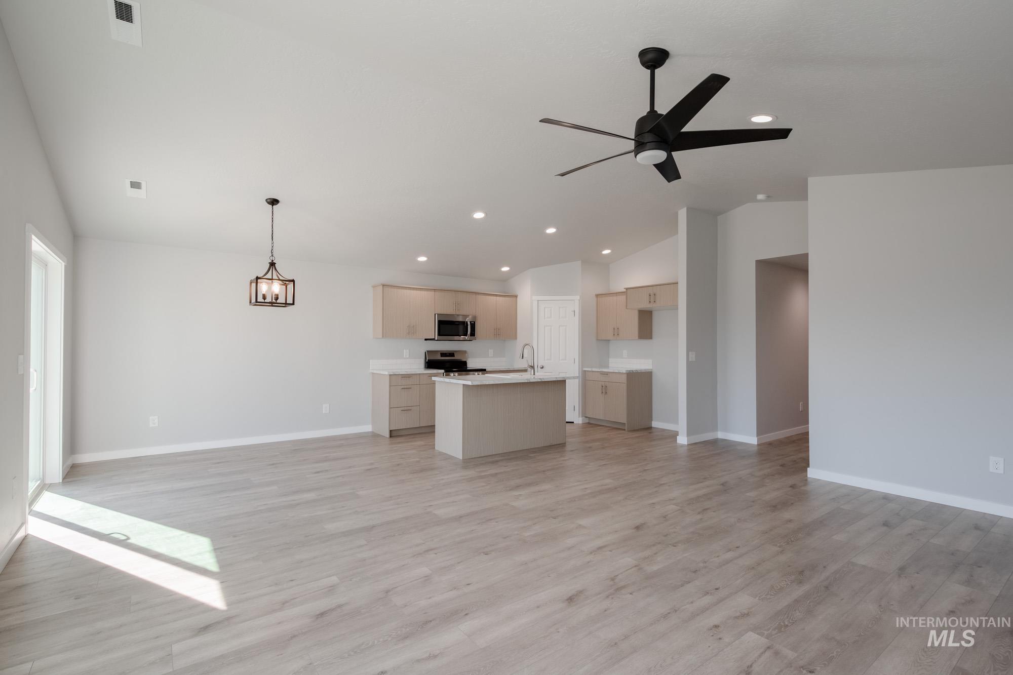 Unfurnished living room featuring lofted ceiling, light wood finished floors, recessed lighting, a chandelier, and ceiling fan