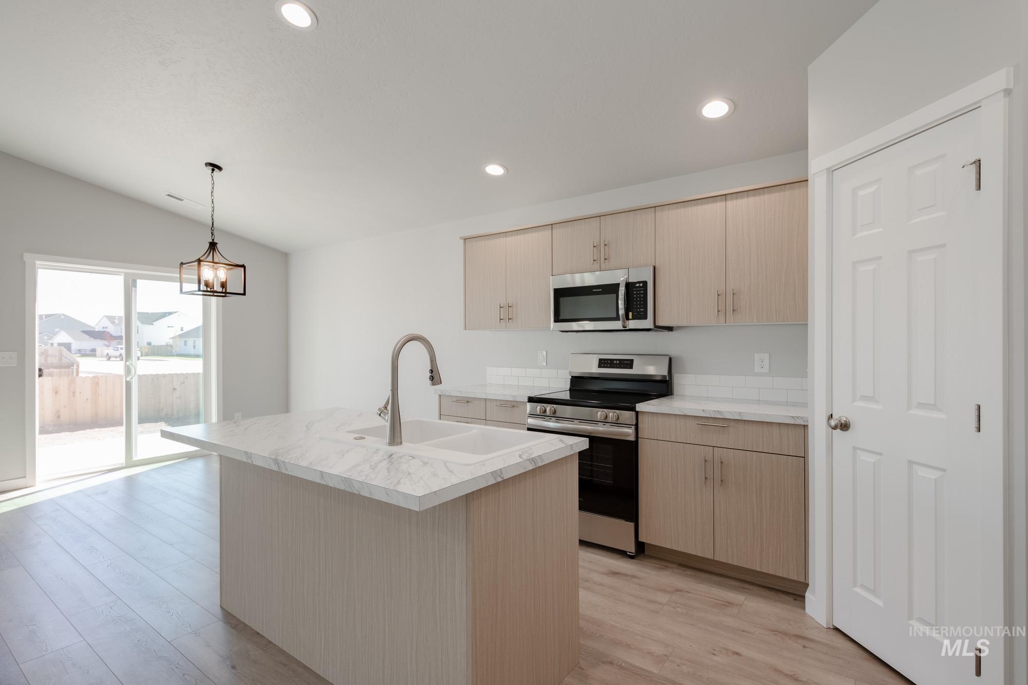 Kitchen with appliances with stainless steel finishes, light countertops, a center island with sink, hanging light fixtures, and light wood-style flooring