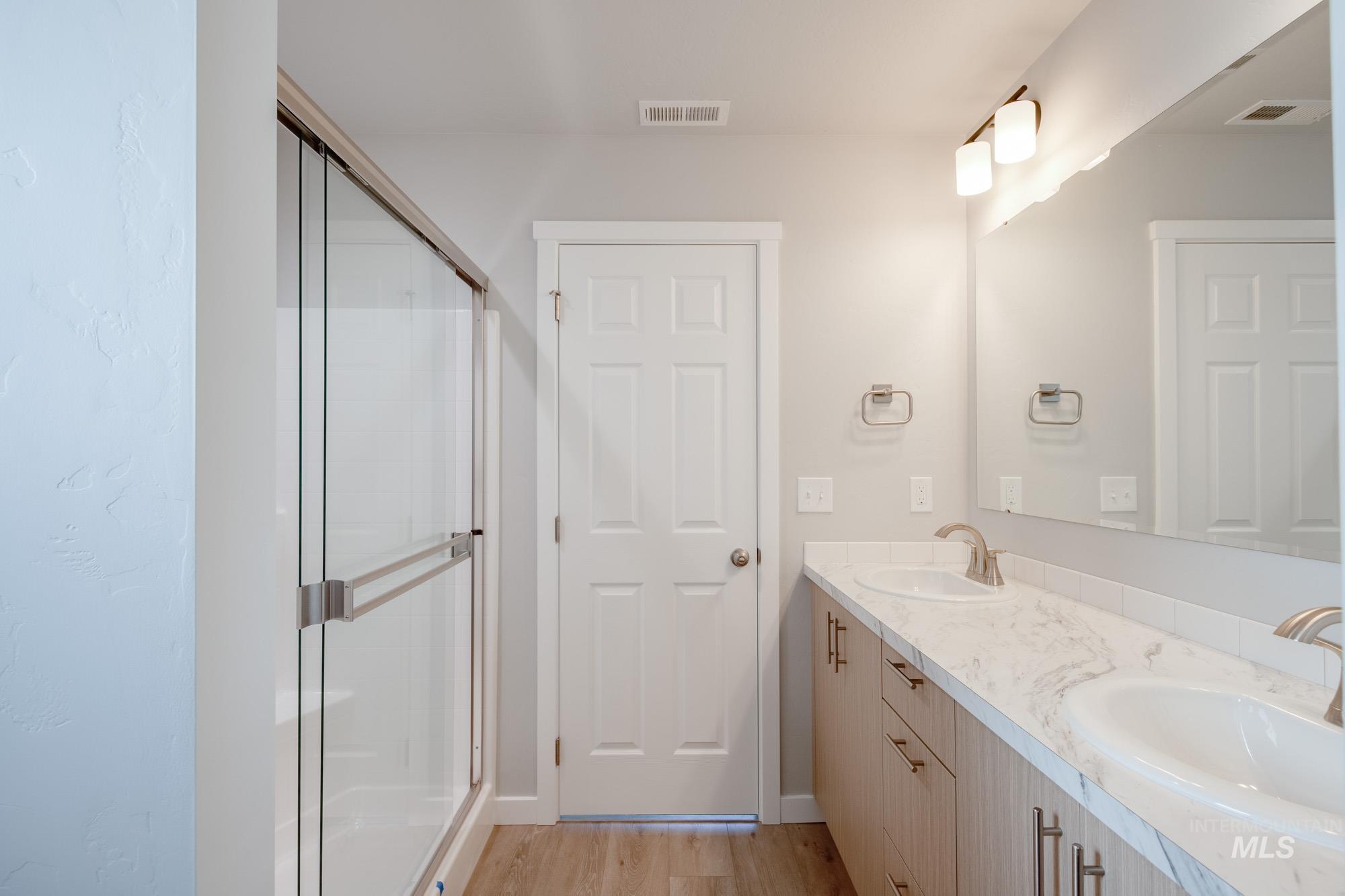 Full bath with light wood-type flooring, a shower stall, and double vanity
