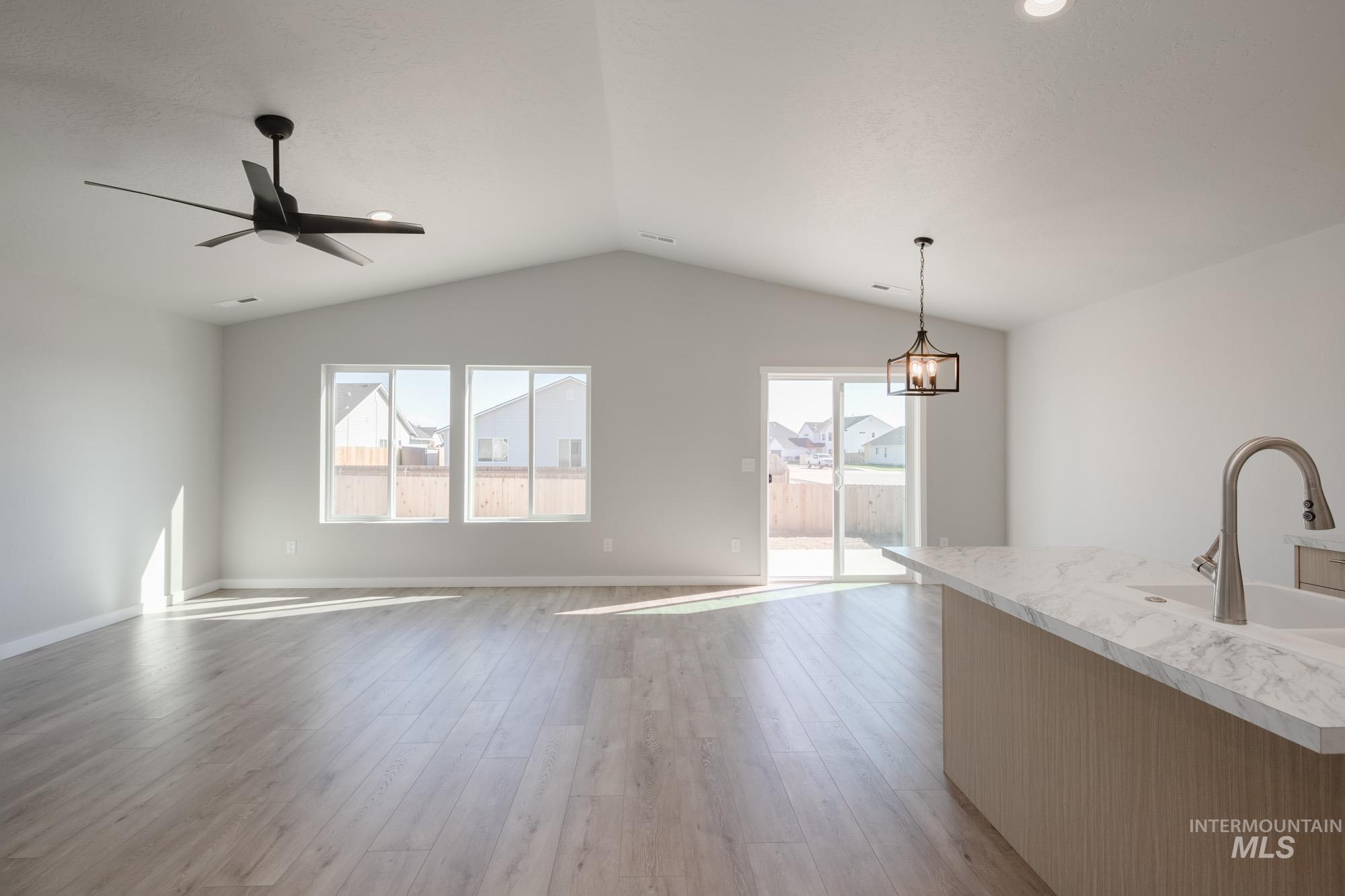 Unfurnished living room featuring light wood-style floors, ceiling fan, and vaulted ceiling