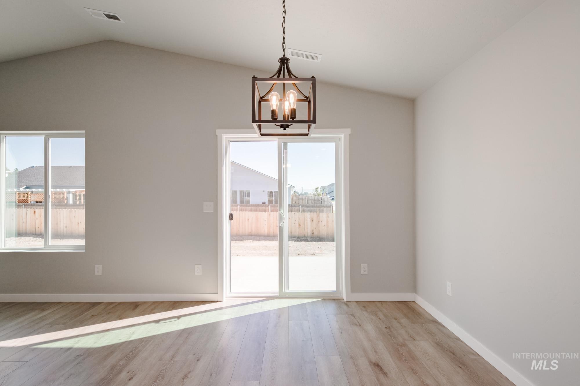 Unfurnished dining area with light wood-style floors, lofted ceiling, and a chandelier