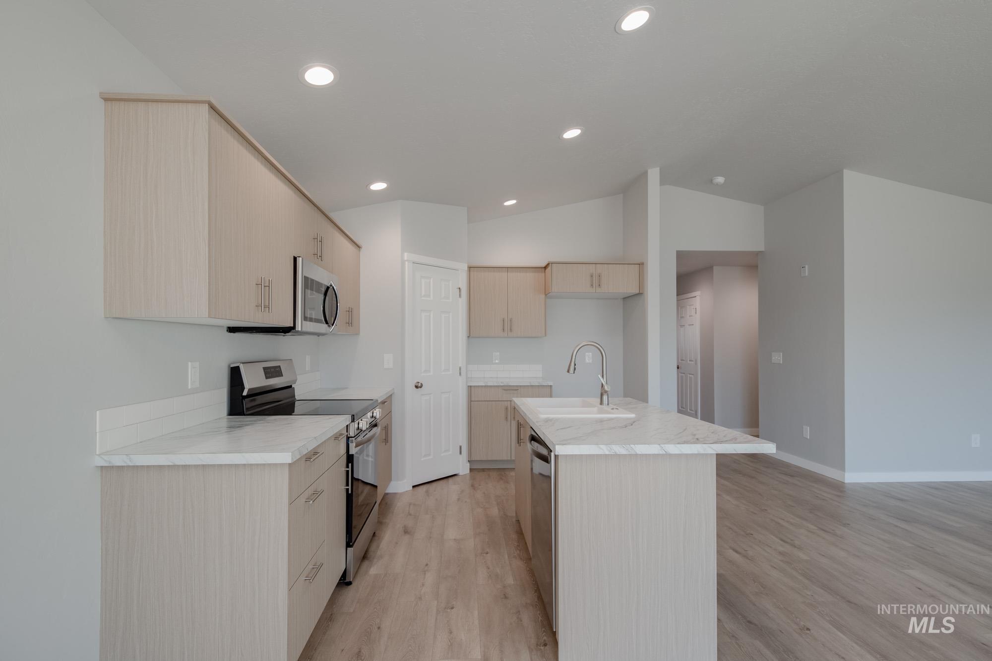 Kitchen with appliances with stainless steel finishes, light wood finished floors, light brown cabinetry, a kitchen island with sink, and vaulted ceiling