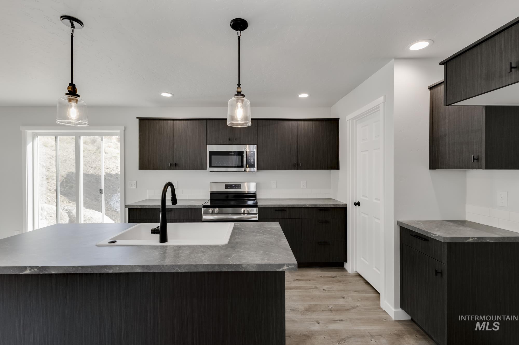 Kitchen featuring appliances with stainless steel finishes, light wood-style floors, decorative light fixtures, an island with sink, and modern cabinets