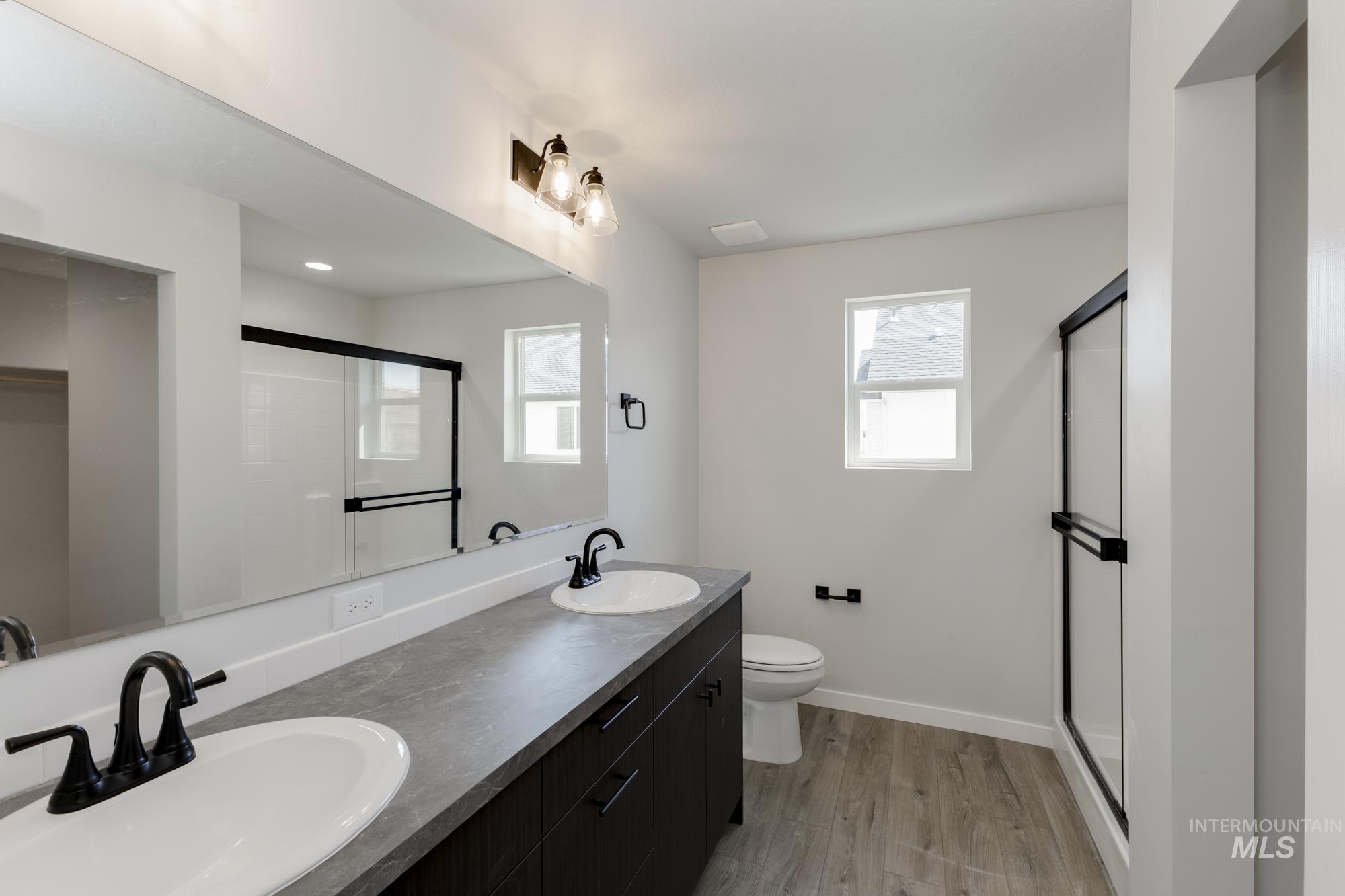 Full bath featuring light wood-style floors, a shower stall, double vanity, and plenty of natural light