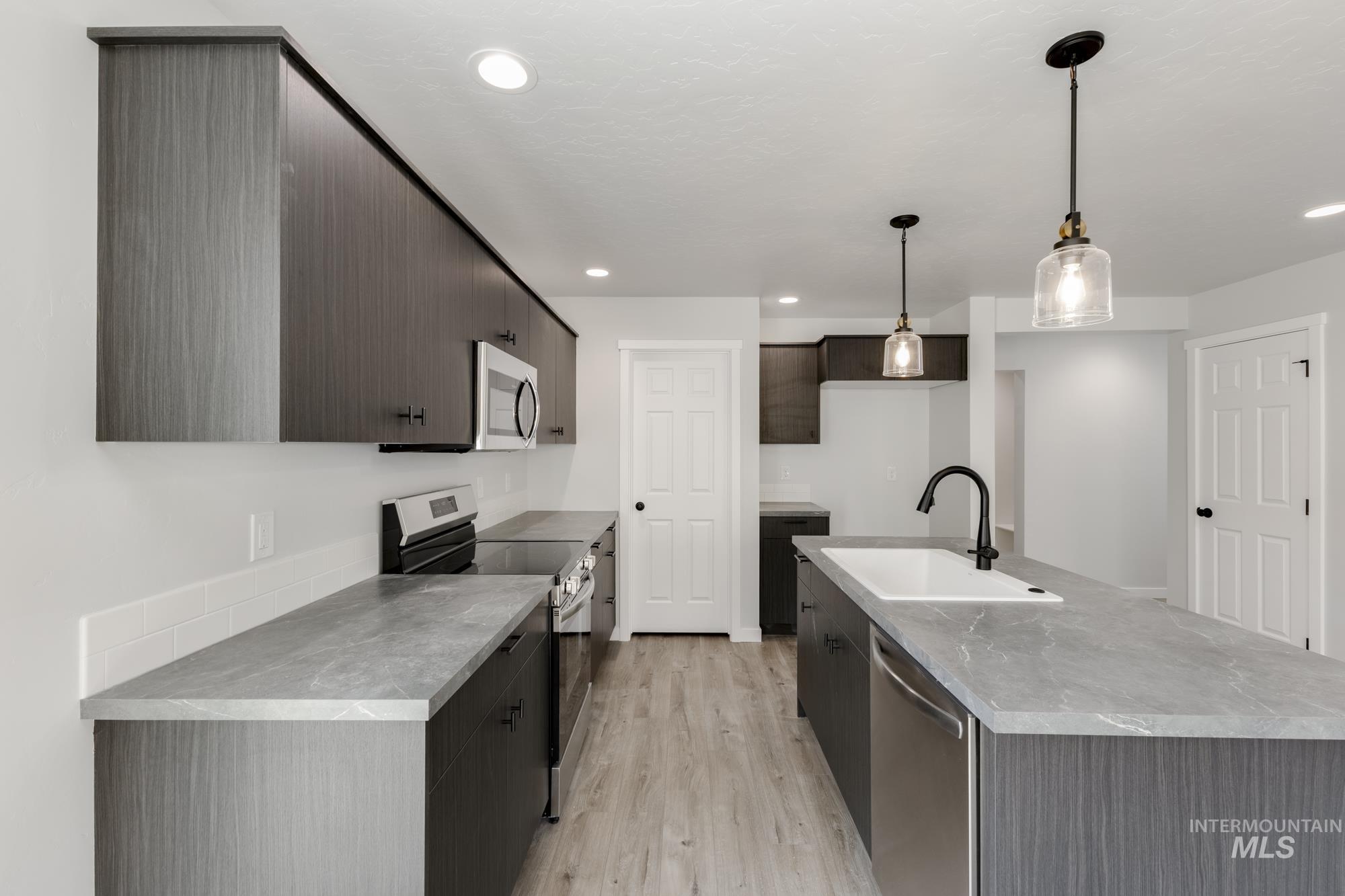 Kitchen with appliances with stainless steel finishes, light wood-style floors, recessed lighting, decorative light fixtures, and a center island with sink