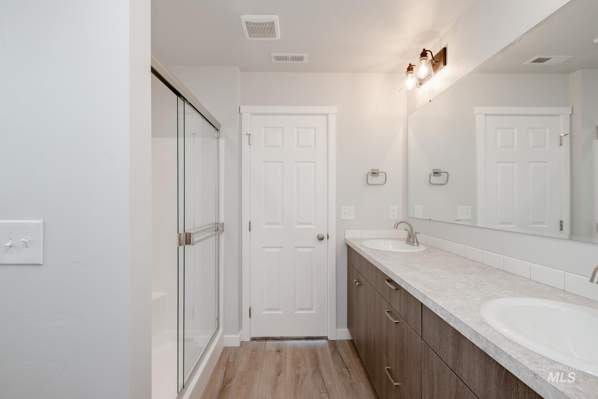 Bathroom featuring light wood-style flooring, a shower stall, and double vanity