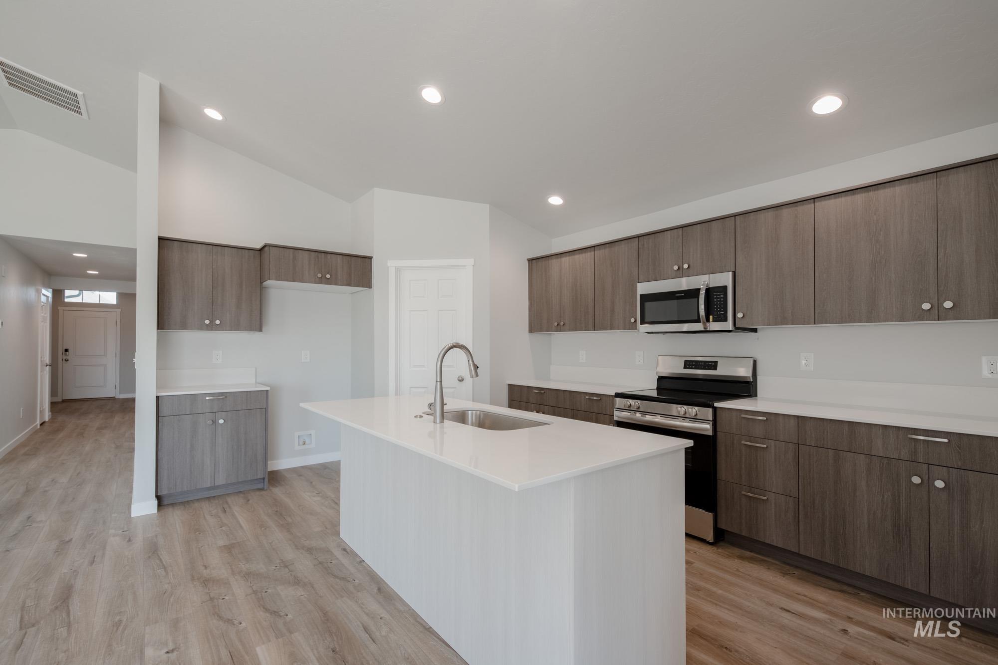 Kitchen featuring stainless steel appliances, vaulted ceiling, light wood-type flooring, recessed lighting, and modern cabinets