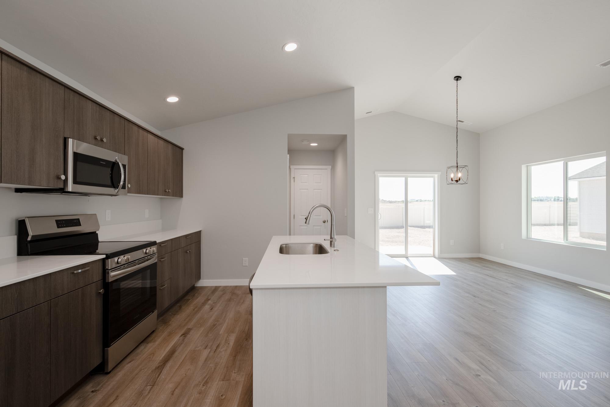 Kitchen with appliances with stainless steel finishes, vaulted ceiling, light wood finished floors, modern cabinets, and an island with sink