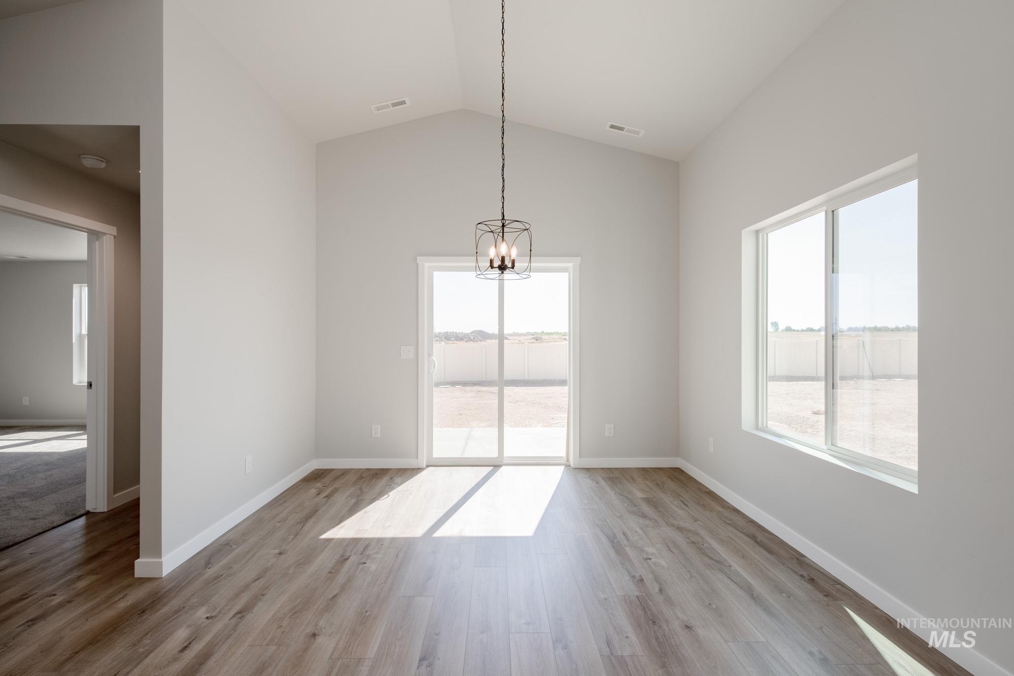 Unfurnished dining area with healthy amount of natural light, vaulted ceiling, light wood finished floors, and a chandelier
