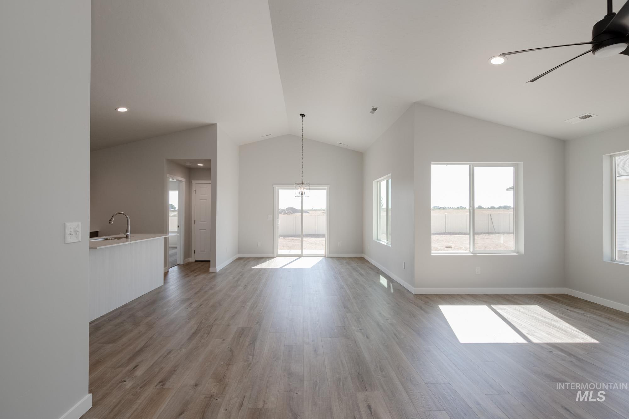 Unfurnished living room featuring light wood-style floors, lofted ceiling, recessed lighting, a ceiling fan, and a chandelier