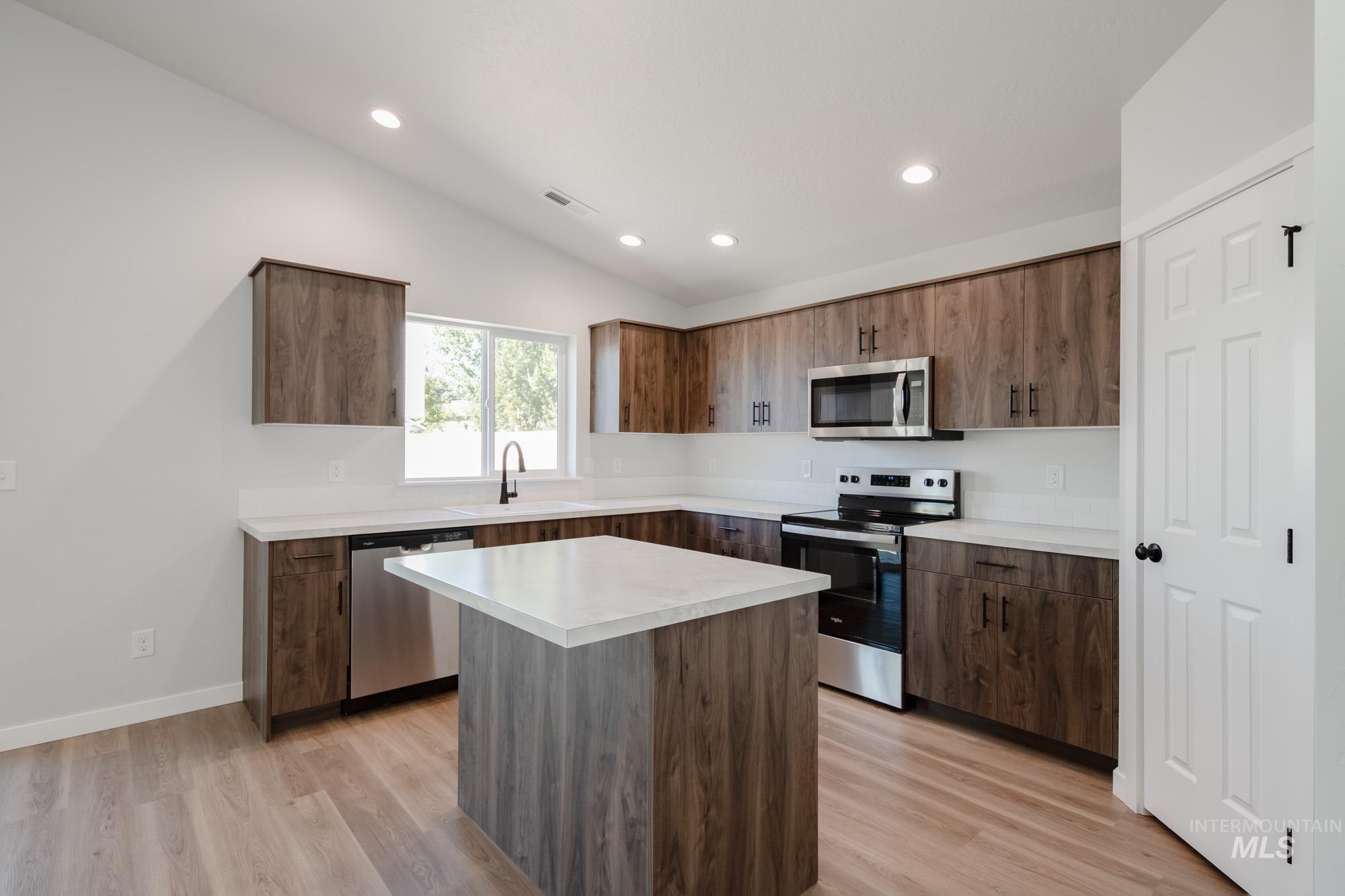 Kitchen featuring appliances with stainless steel finishes, light countertops, vaulted ceiling, light wood-style floors, and a kitchen island