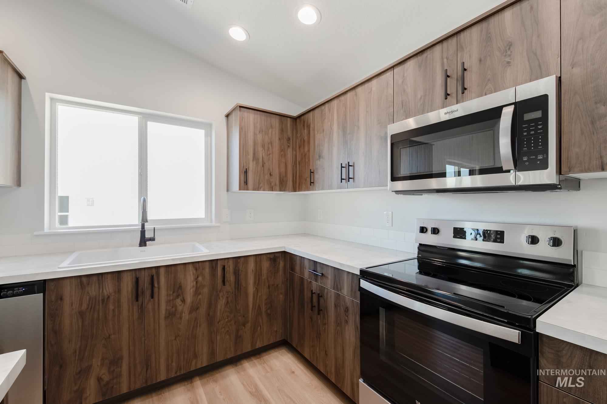 Kitchen featuring appliances with stainless steel finishes, light countertops, light wood finished floors, vaulted ceiling, and recessed lighting