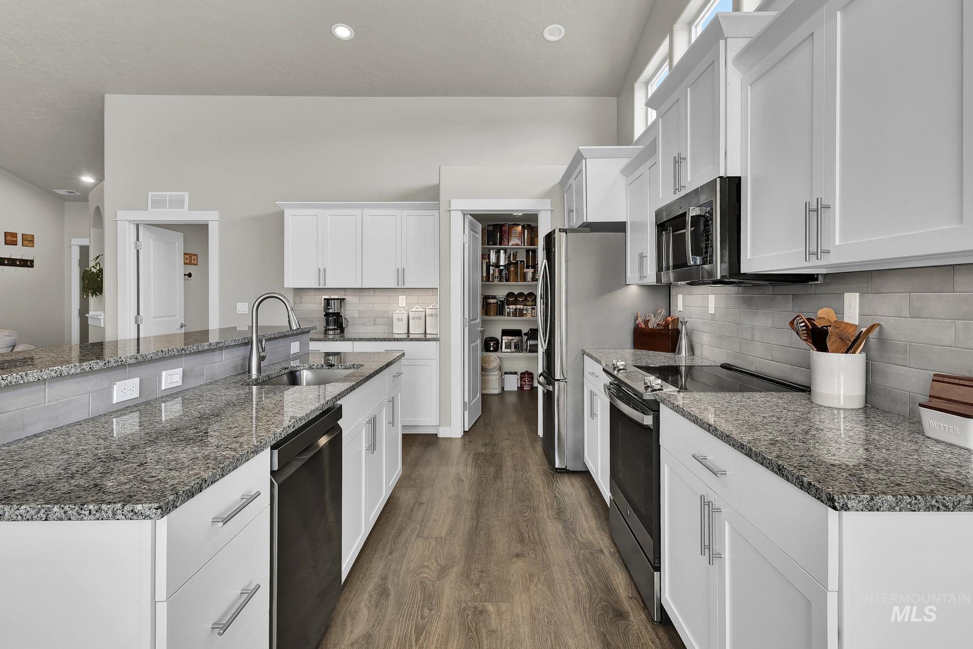 Kitchen with appliances with stainless steel finishes, dark stone countertops, white cabinets, dark wood-type flooring, and recessed lighting