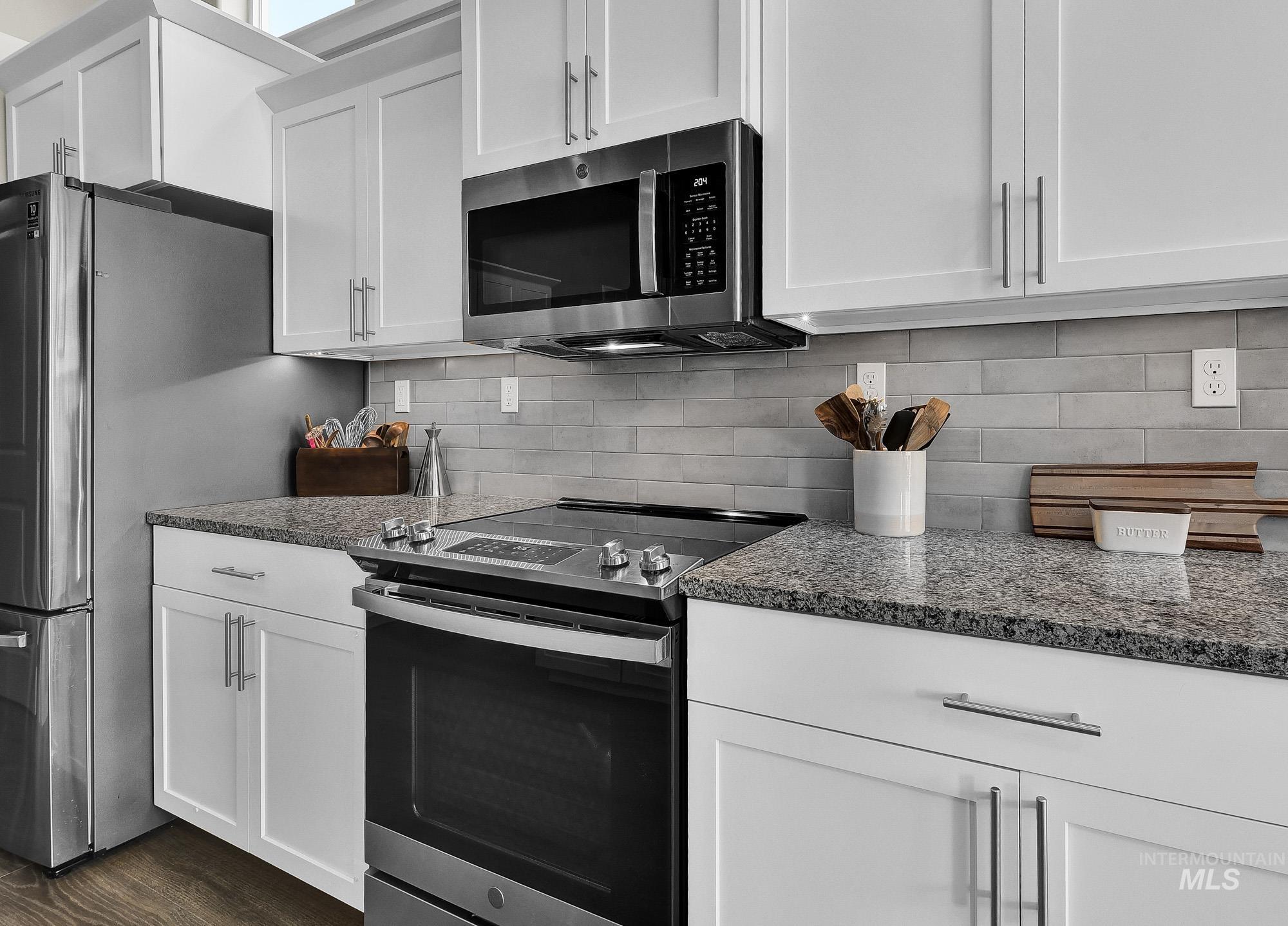 Kitchen featuring stainless steel appliances, white cabinetry, backsplash, and dark stone counters