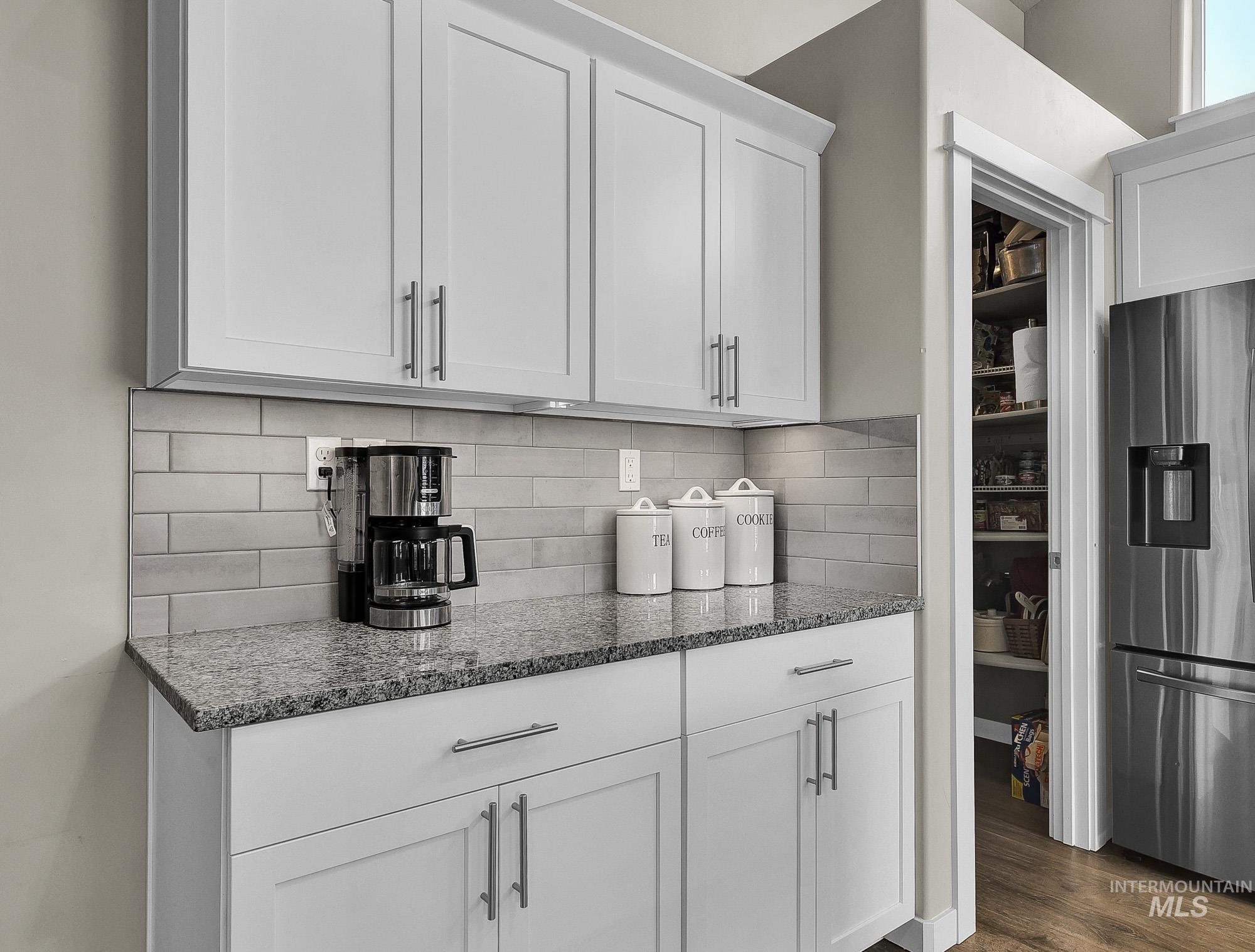 Kitchen featuring stainless steel fridge with ice dispenser, dark stone counters, white cabinetry, dark wood-type flooring, and tasteful backsplash