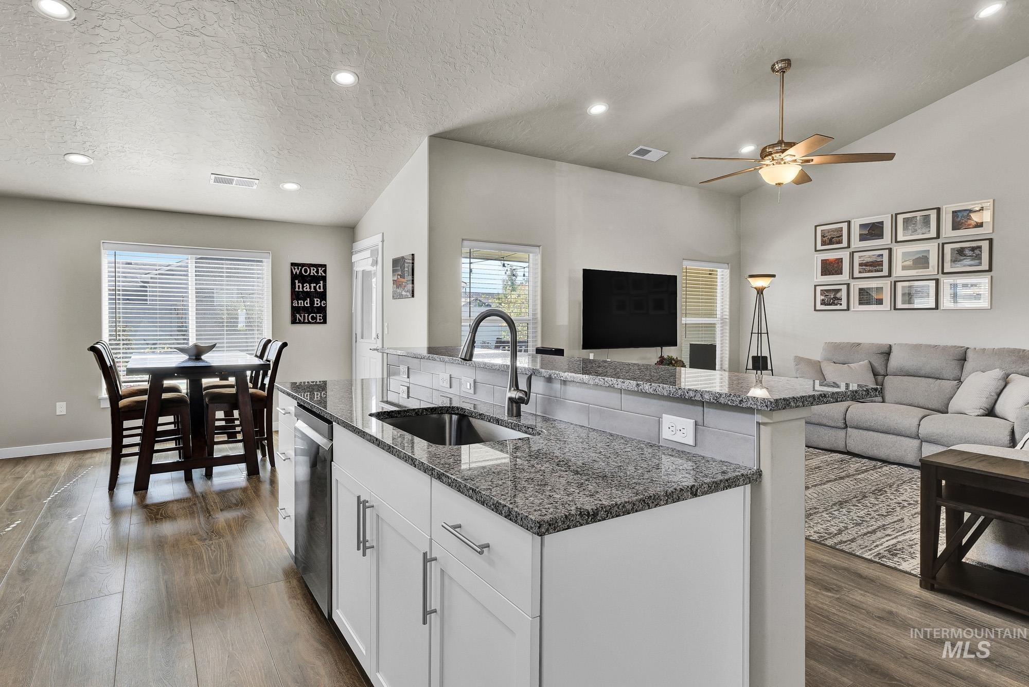 Kitchen featuring a textured ceiling, white cabinets, dark stone counters, an island with sink, and recessed lighting