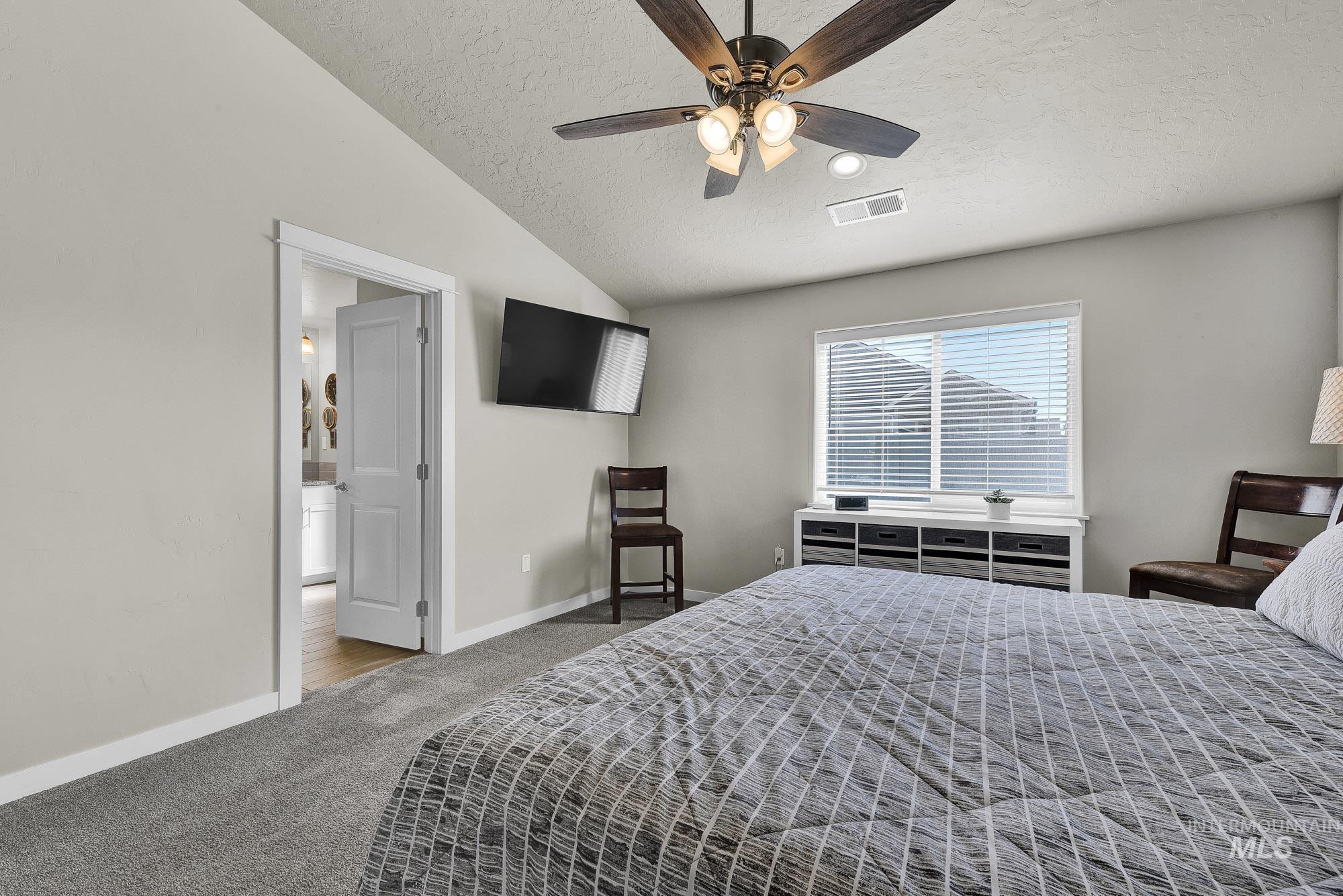 Carpeted bedroom featuring lofted ceiling, a textured ceiling, and a ceiling fan