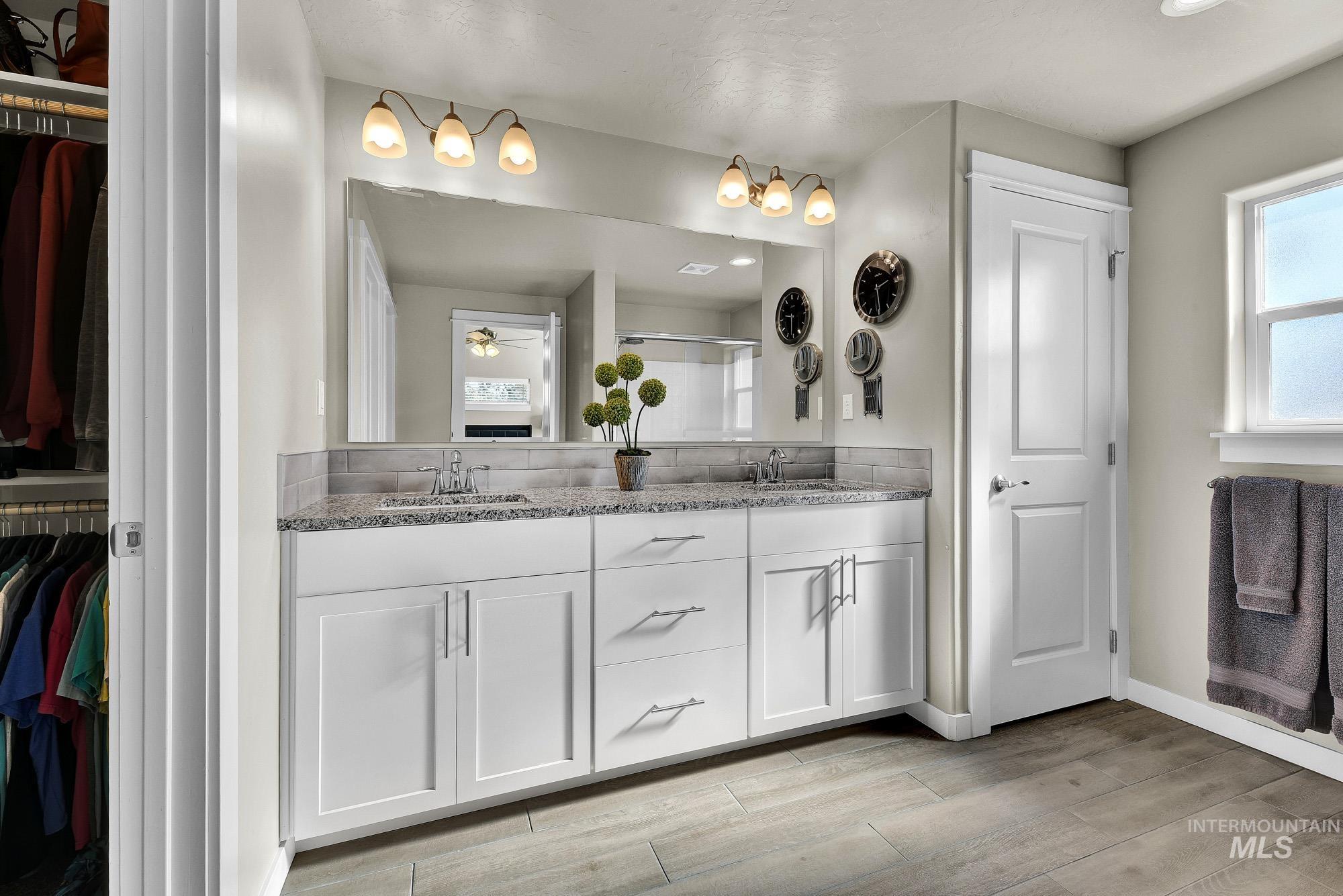Bathroom featuring a walk in closet, double vanity, a shower stall, and light wood finished floors