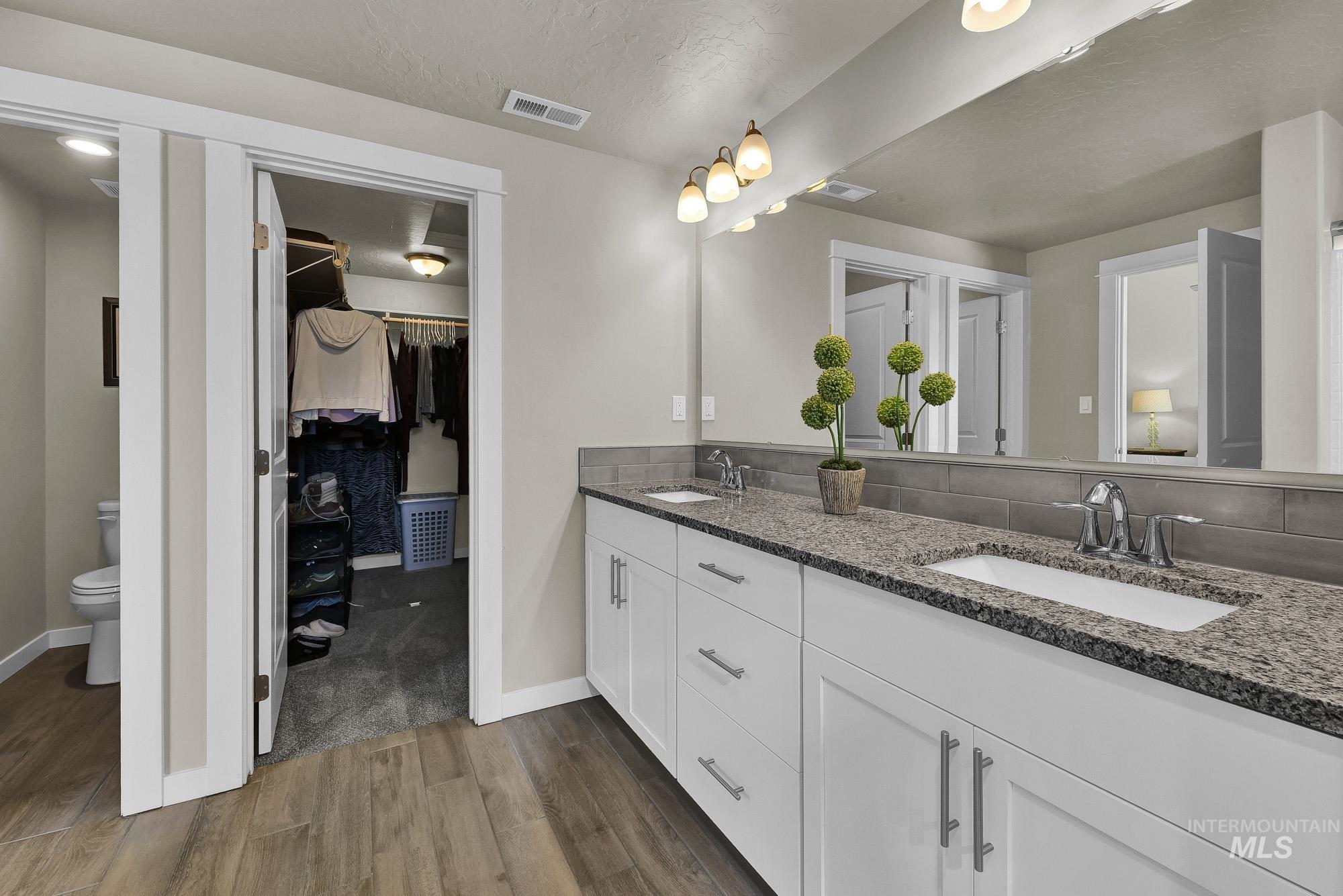 Bathroom with dark wood-type flooring, a walk in closet, double vanity, and a textured ceiling