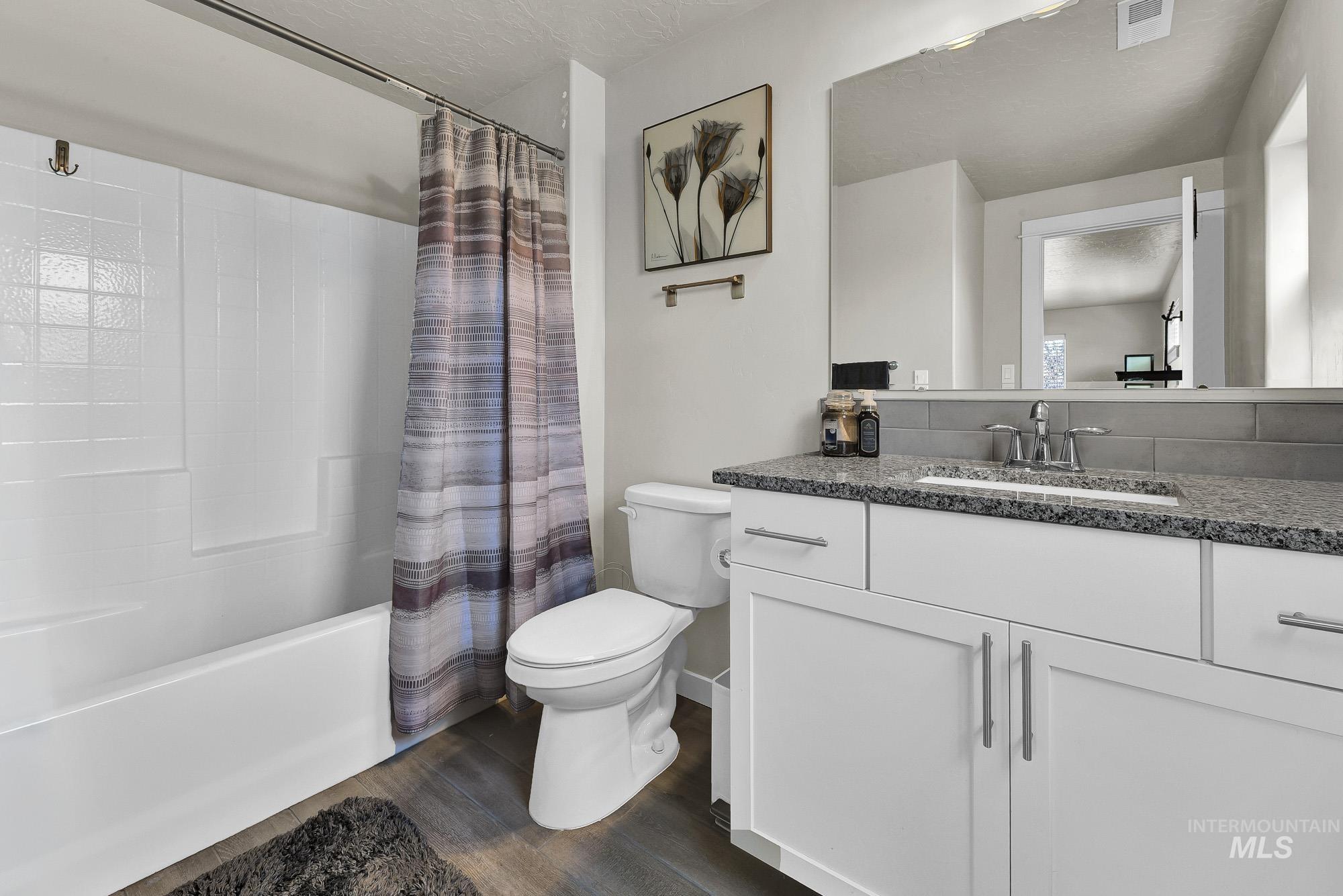 Full bathroom featuring shower / tub combo with curtain, vanity, dark wood-style floors, and a textured ceiling