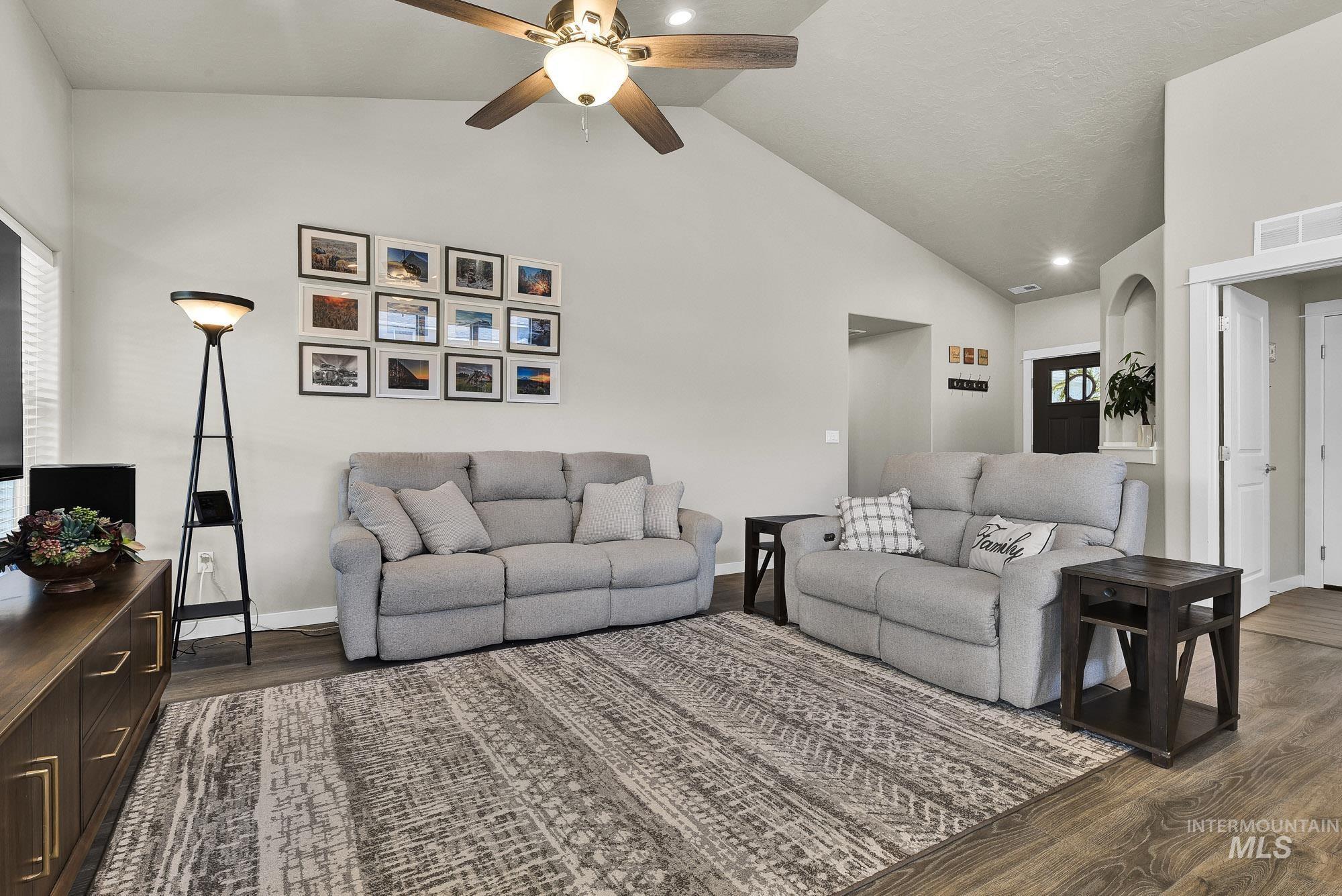 Living room with dark wood finished floors, healthy amount of natural light, a ceiling fan, and high vaulted ceiling
