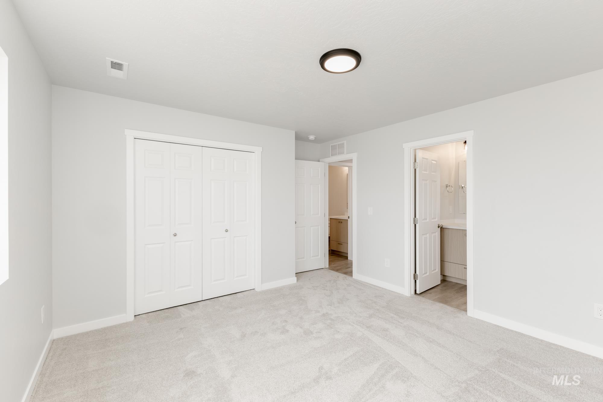 Unfurnished bedroom featuring light colored carpet, a closet, and ensuite bathroom