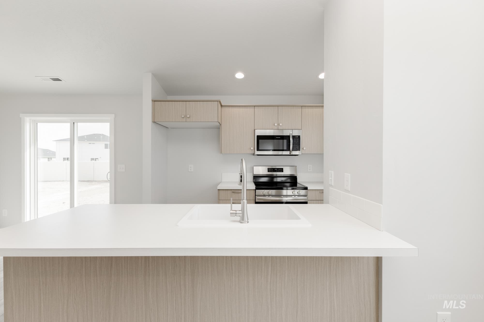 Kitchen with light brown cabinetry, a peninsula, appliances with stainless steel finishes, recessed lighting, and modern cabinets