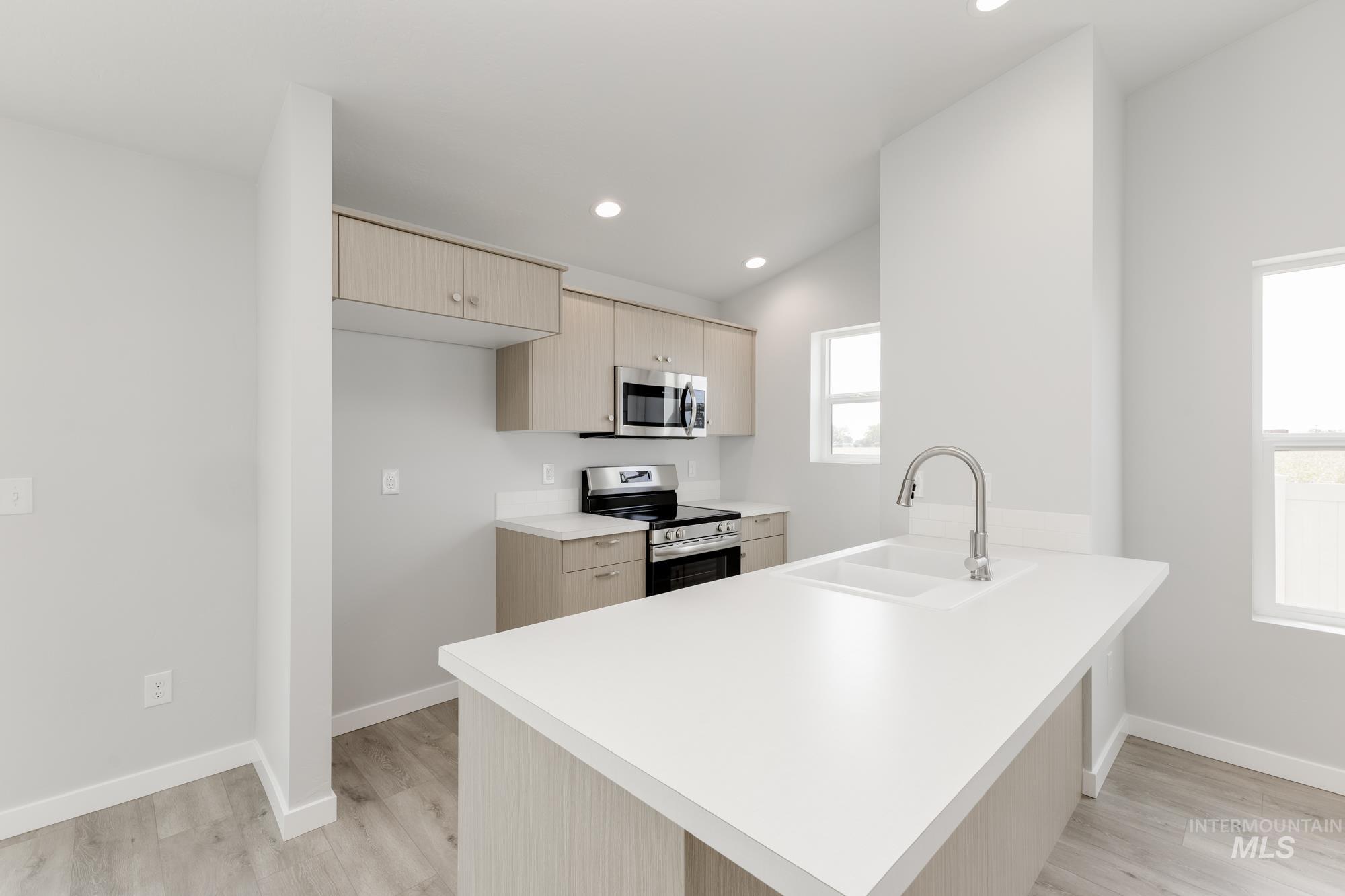 Kitchen with stainless steel appliances, light countertops, a peninsula, light brown cabinetry, and light wood finished floors