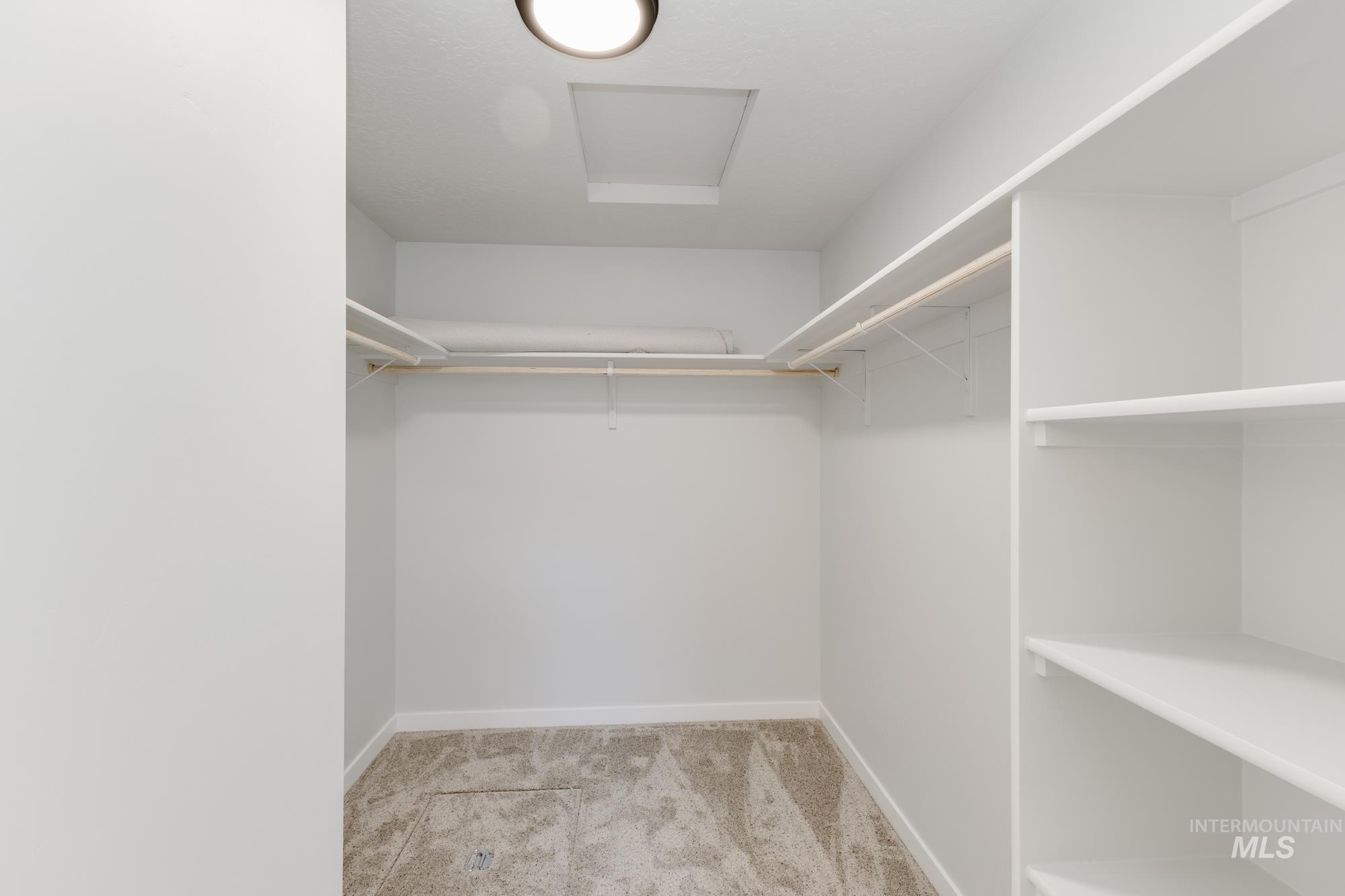 Walk in closet with light carpet and attic access