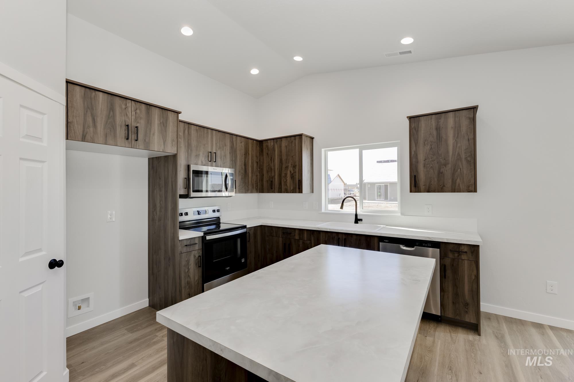 Kitchen featuring appliances with stainless steel finishes, light countertops, dark brown cabinetry, light wood-style flooring, and lofted ceiling