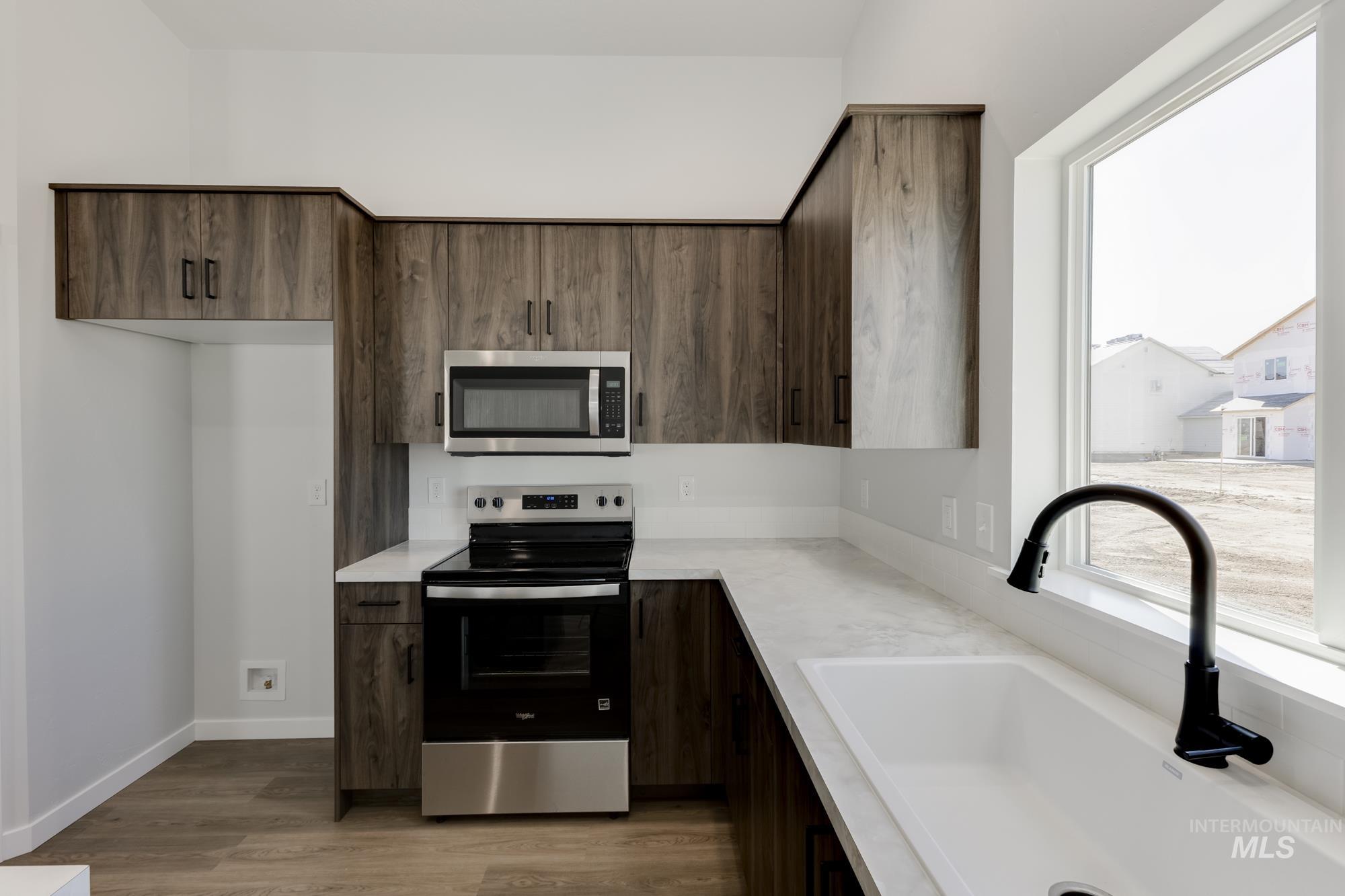 Kitchen with appliances with stainless steel finishes, dark brown cabinets, and light wood-style flooring