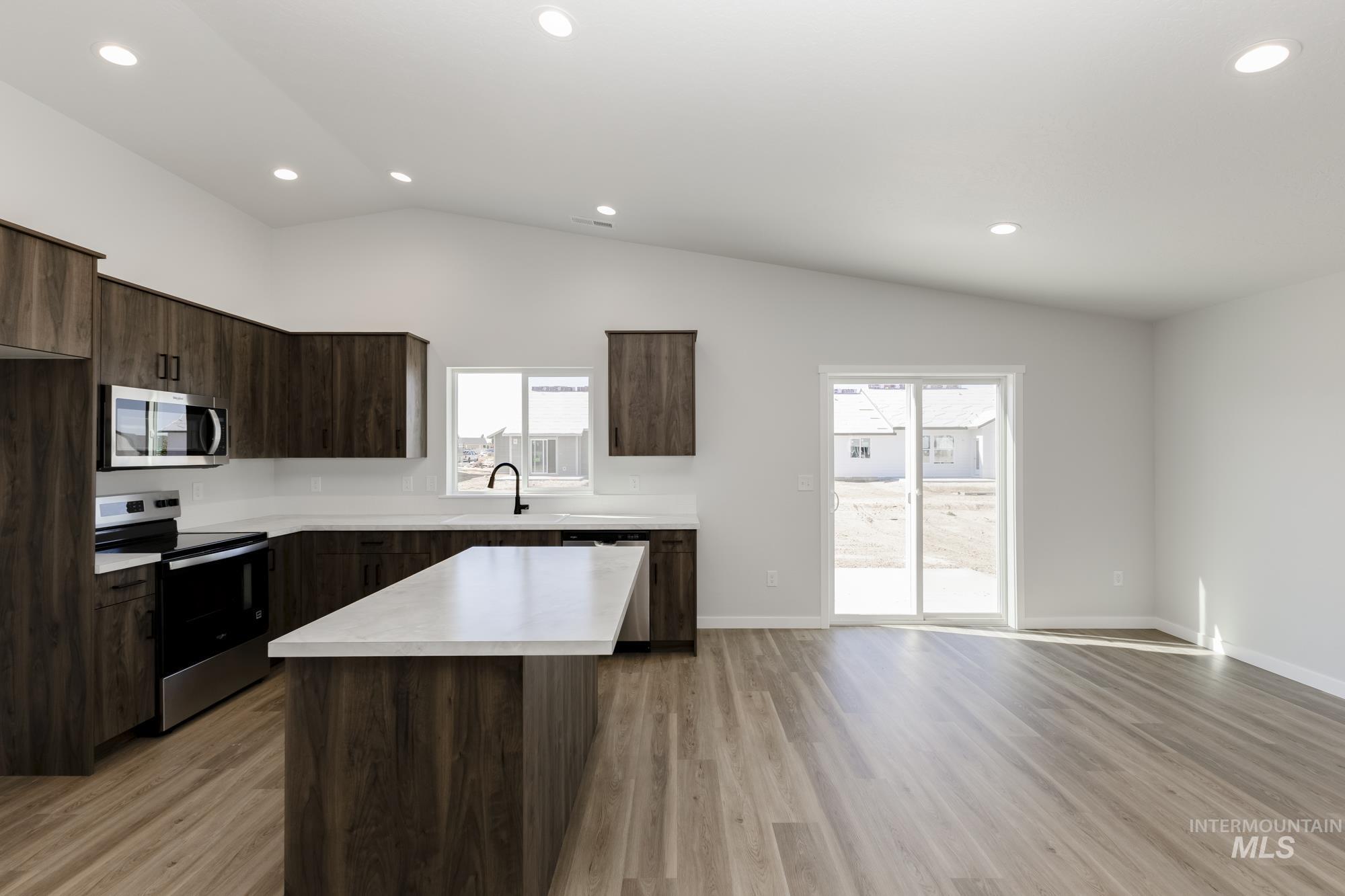 Kitchen with dark brown cabinets, appliances with stainless steel finishes, light countertops, light wood-style floors, and modern cabinets