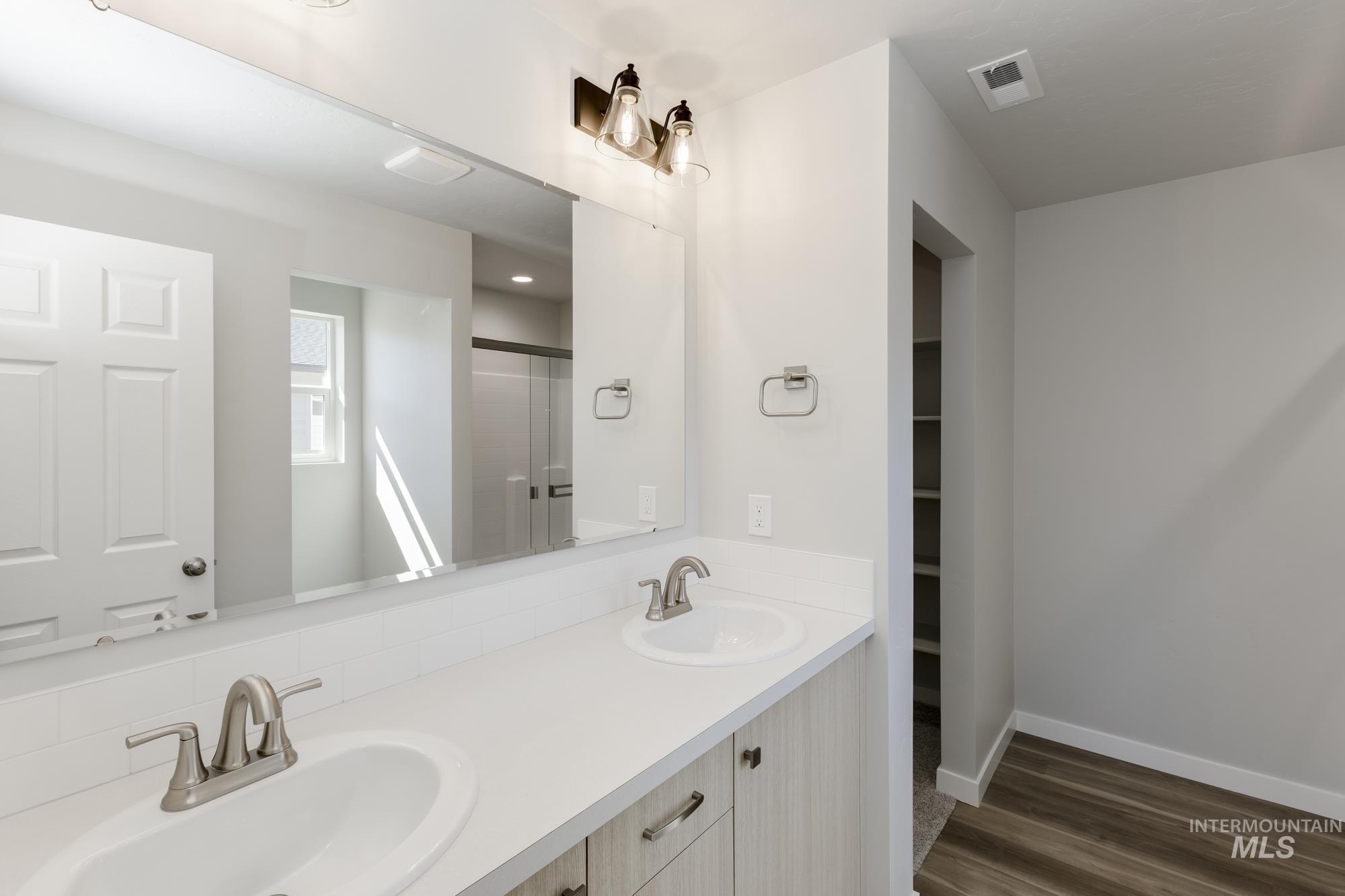 Bathroom featuring a shower with door, double vanity, dark wood-style flooring, and a spacious closet