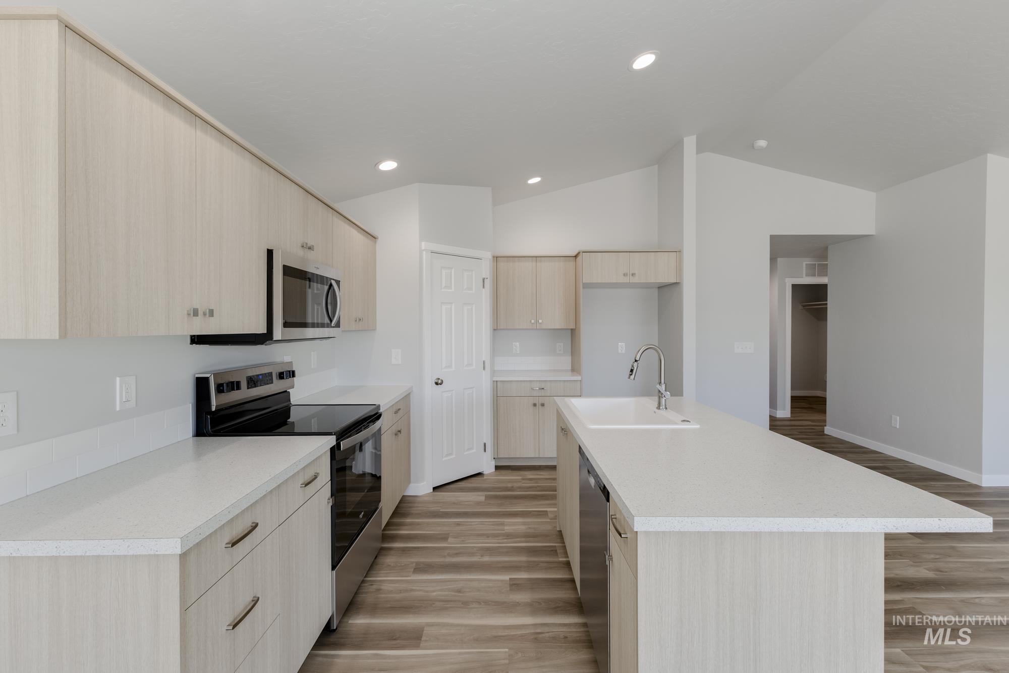 Kitchen with light brown cabinetry, stainless steel appliances, light wood-style flooring, a kitchen island with sink, and lofted ceiling