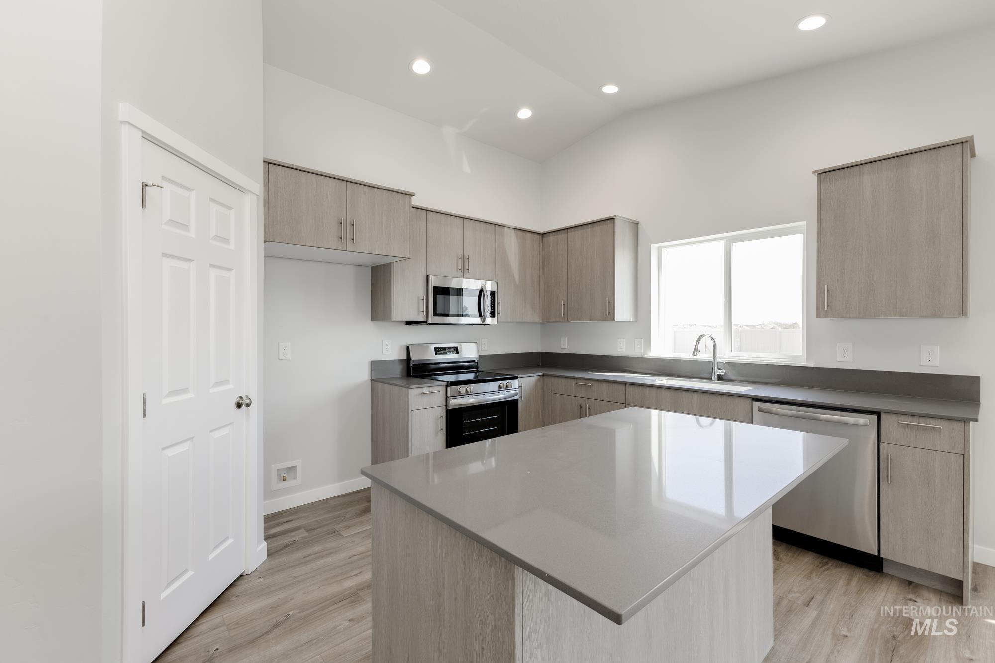 Kitchen with light brown cabinetry, stainless steel appliances, modern cabinets, a kitchen island, and light wood-style flooring