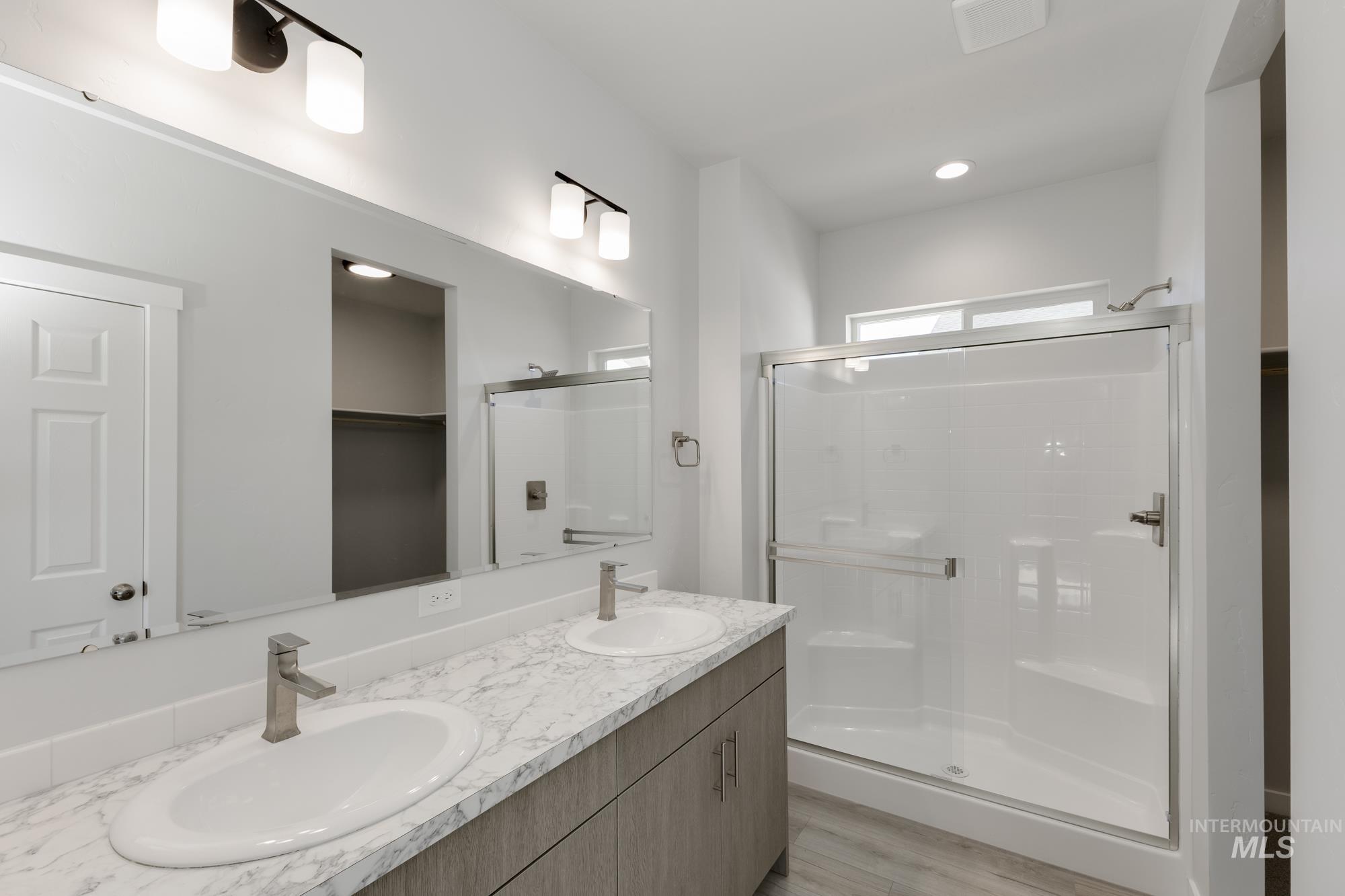Full bathroom featuring a shower stall, double vanity, light wood-type flooring, recessed lighting, and a walk in closet