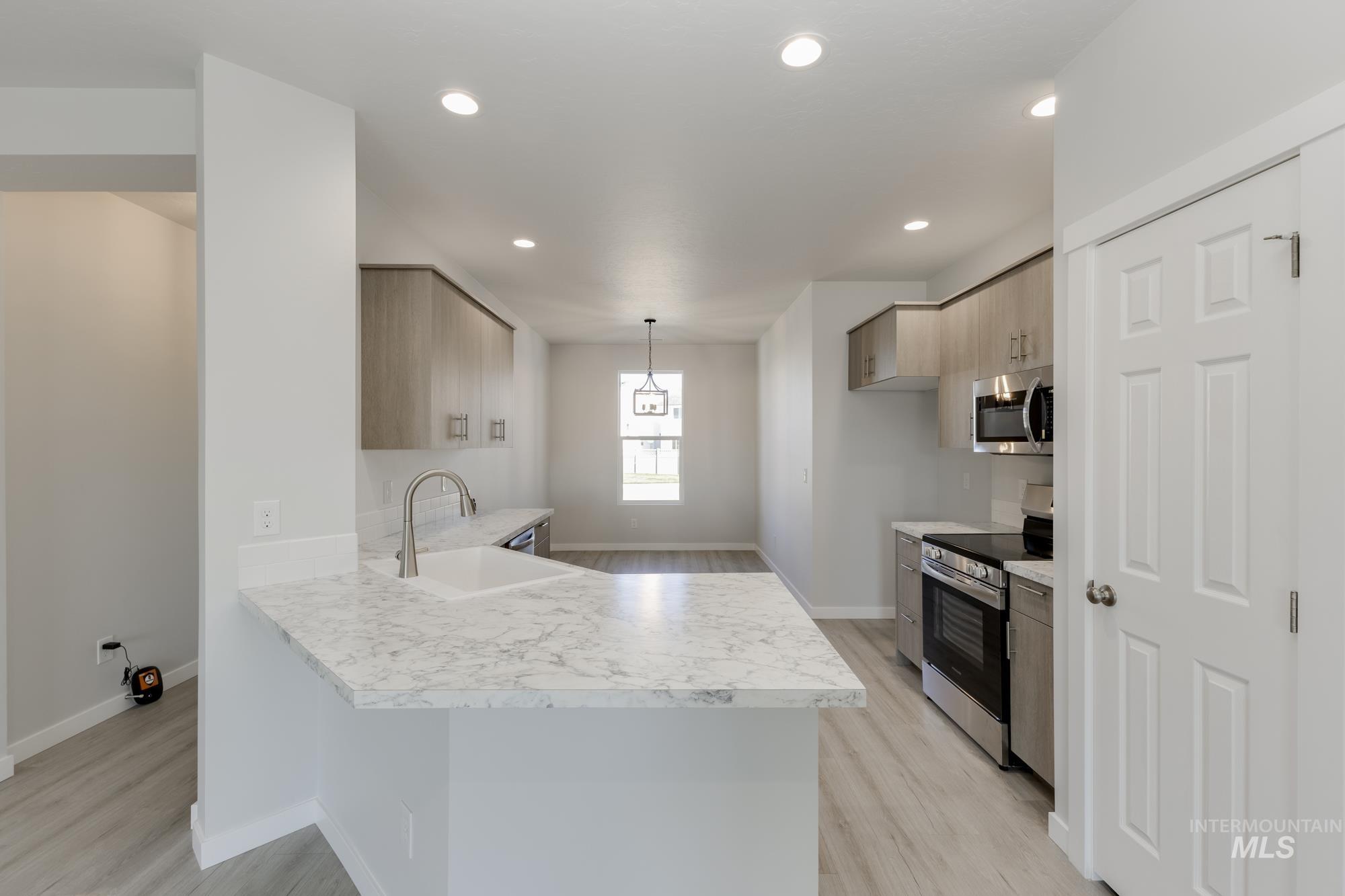 Kitchen featuring light countertops, appliances with stainless steel finishes, a peninsula, light wood finished floors, and recessed lighting