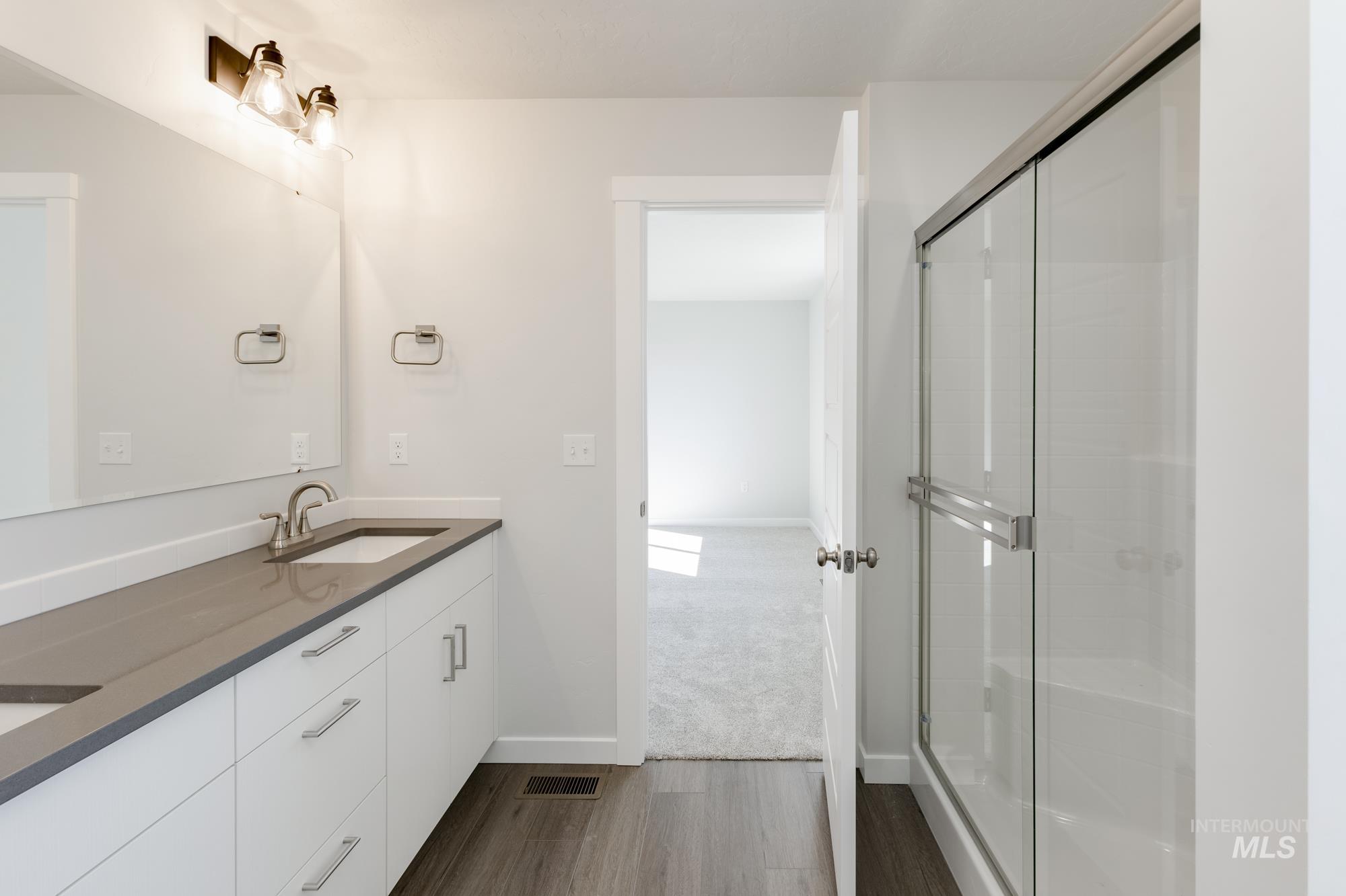 Full bath featuring double vanity, dark wood finished floors, and a shower stall