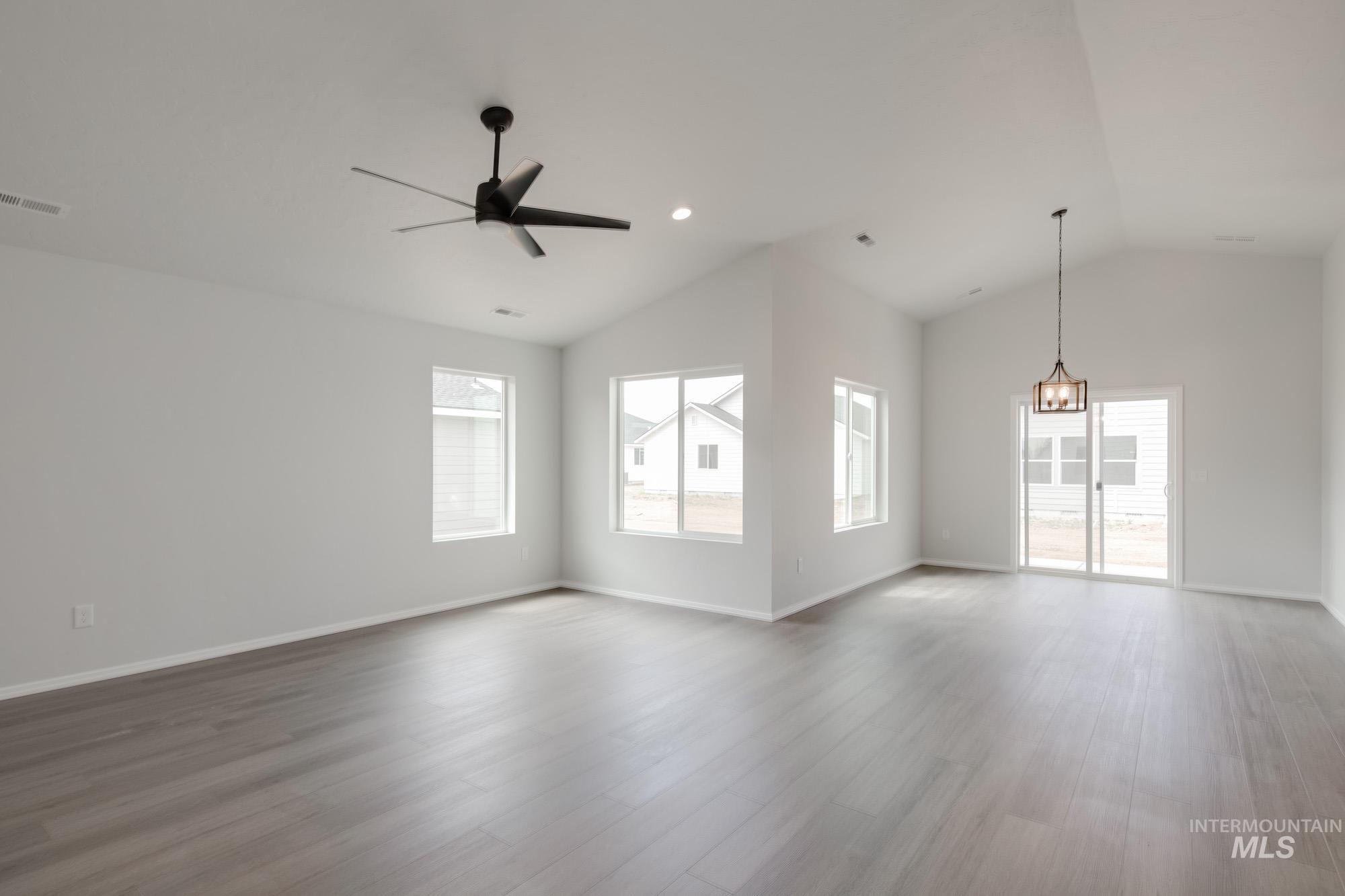 Unfurnished living room with healthy amount of natural light, lofted ceiling, wood finished floors, ceiling fan, and recessed lighting