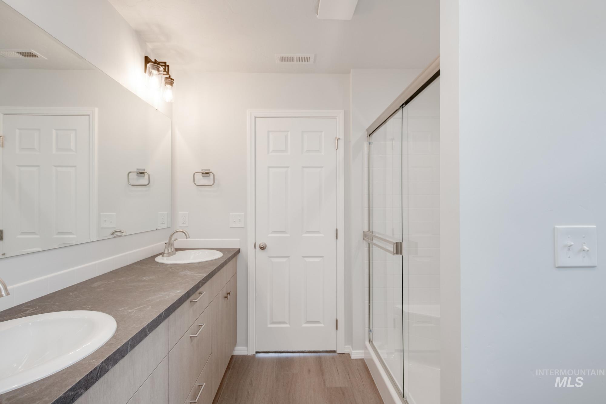 Bathroom with a stall shower, double vanity, and light wood finished floors