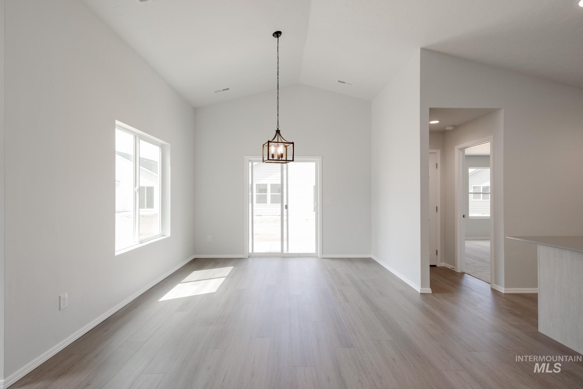 Unfurnished dining area with lofted ceiling, healthy amount of natural light, light wood-style floors, and a chandelier