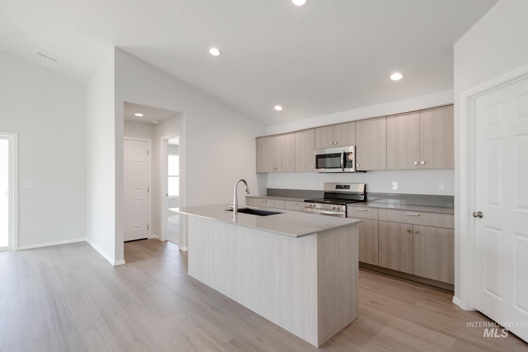 Kitchen featuring light brown cabinets, an island with sink, vaulted ceiling, recessed lighting, and stainless steel appliances